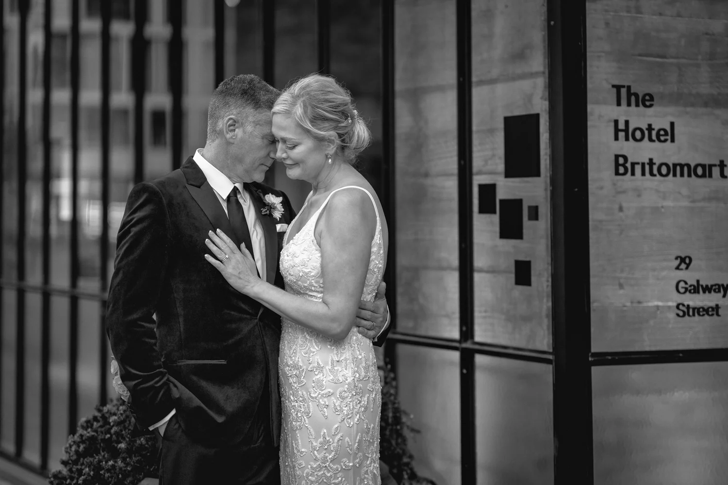 Black and white photo of the couple embracing by the entrance