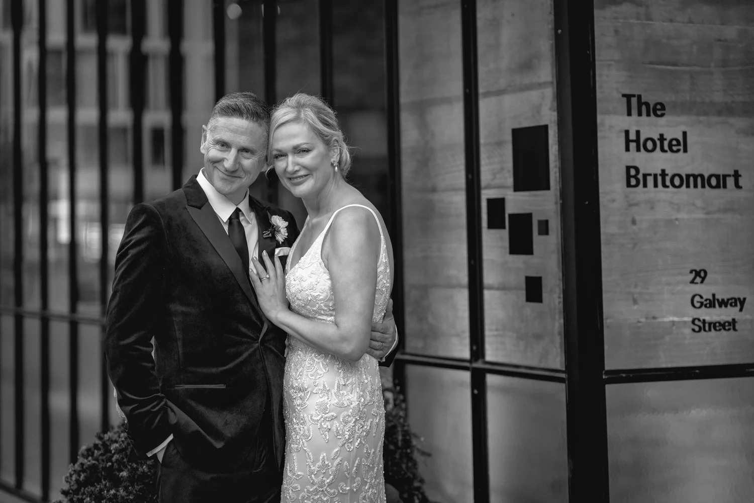 Black and white photo of the couple smiling by the hotel sign