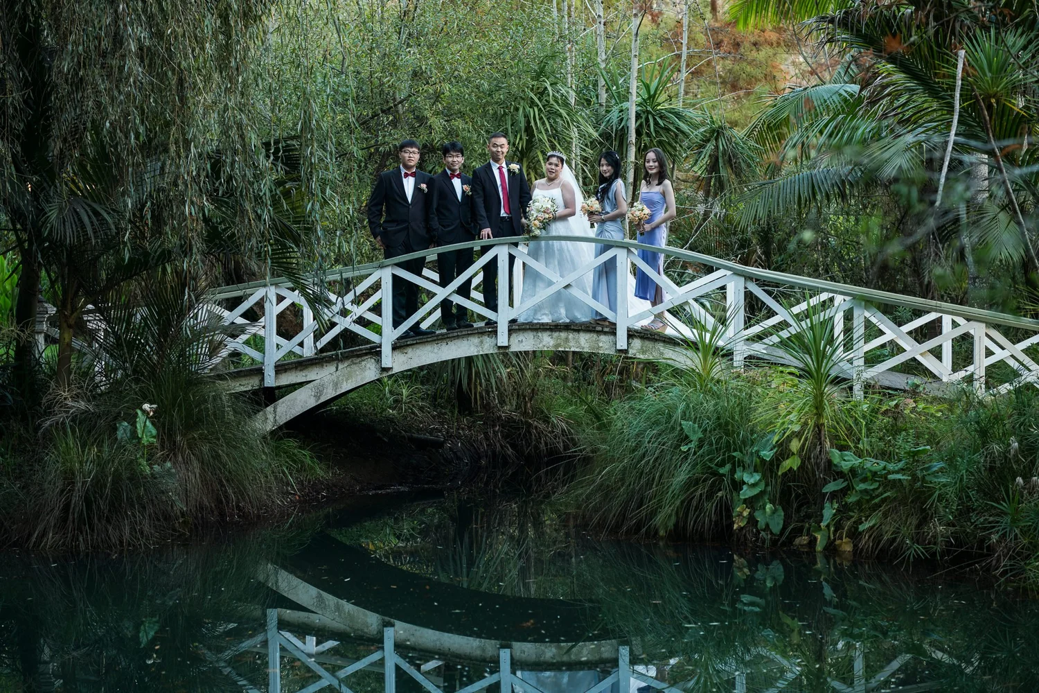 The bridal party on a white bridge reflected in the pond at Settlers Country Manor