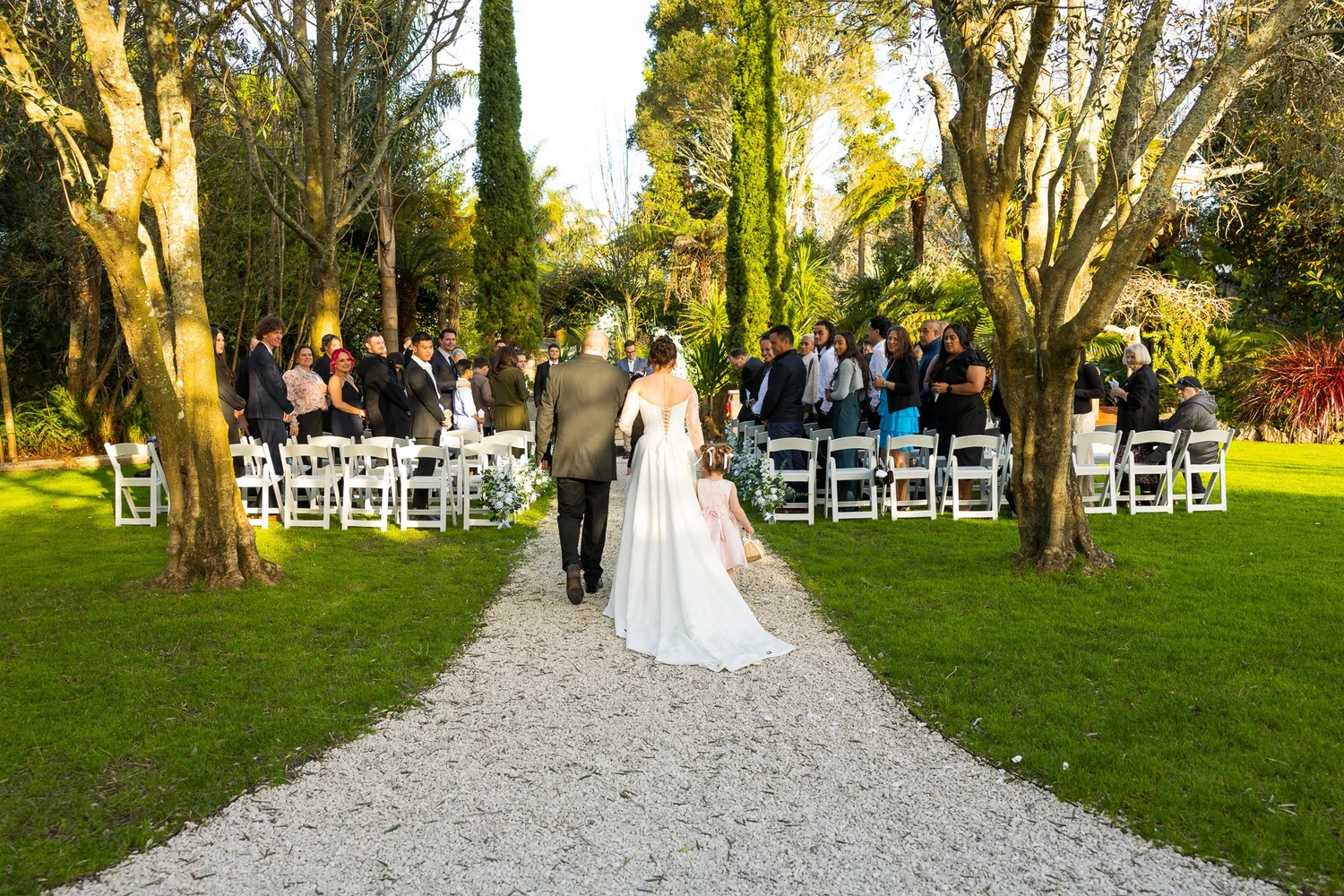 A couple walk down the gravel aisle towards their guests