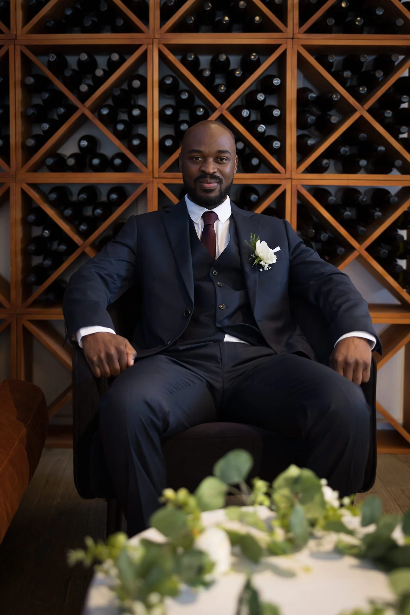 Foster seated in an armchair in front of a wine rack