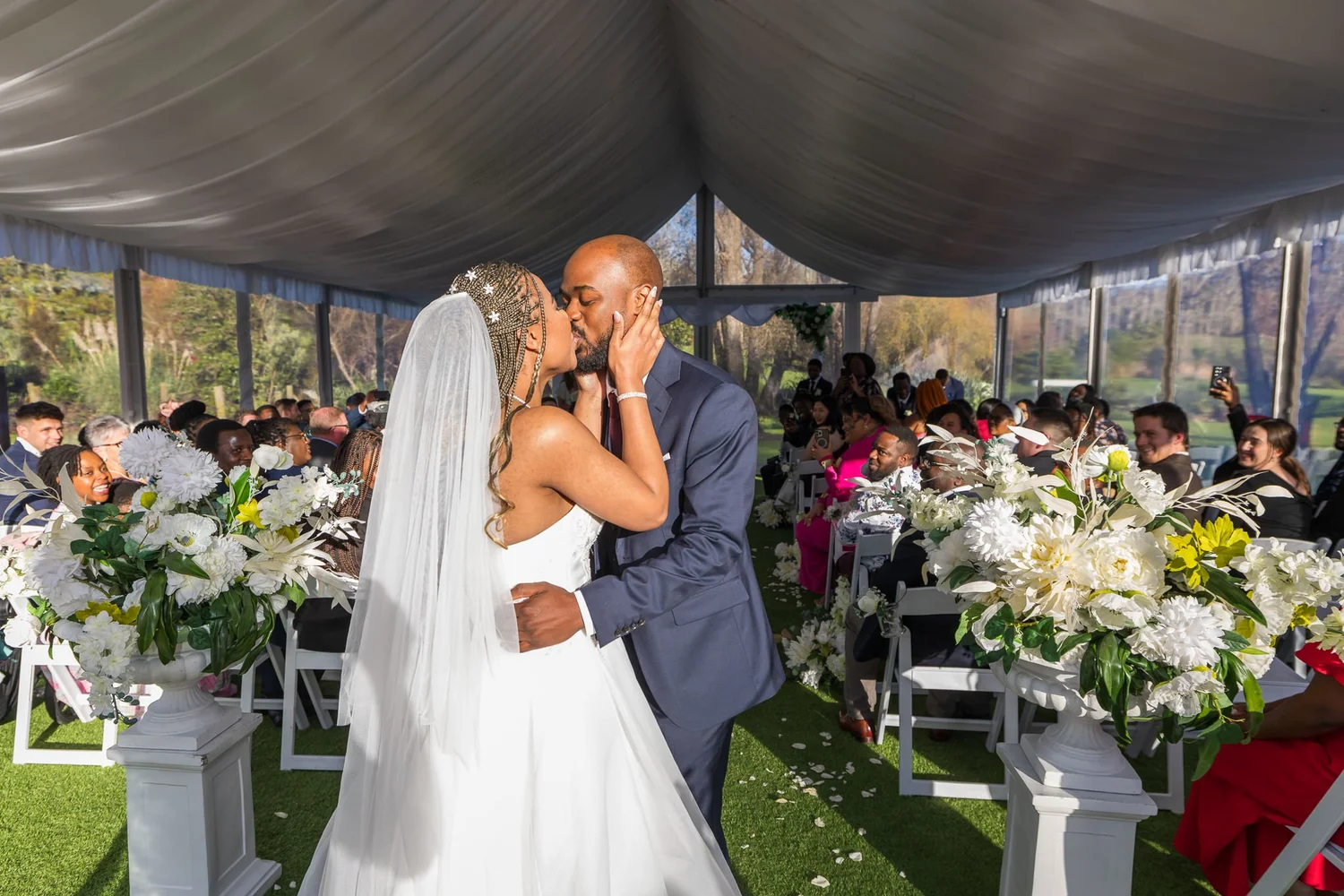 Chiedza and Foster kiss at the end of the aisle in the marquee
