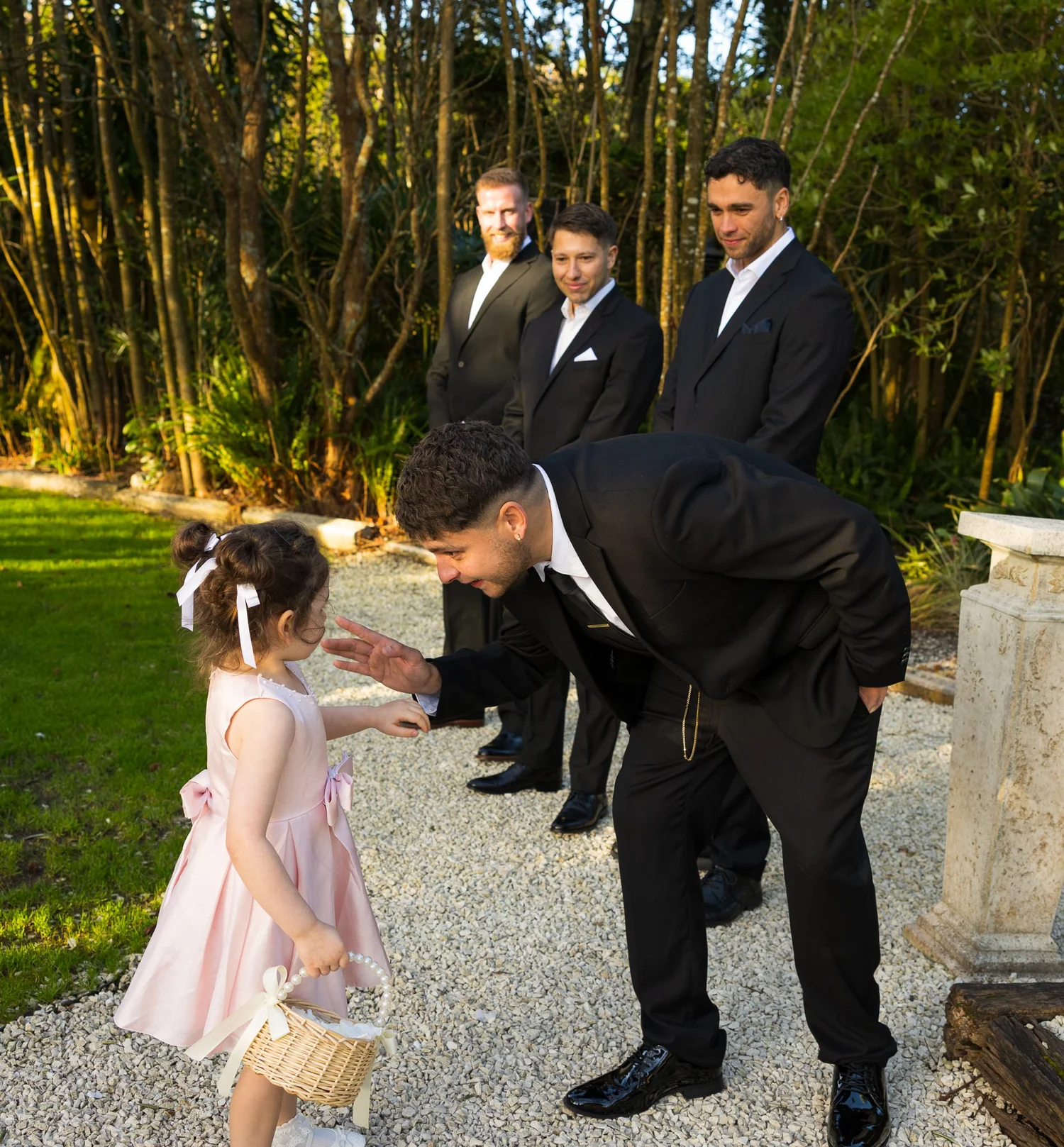 A groomsman bends down to greet a flower girl before the ceremony