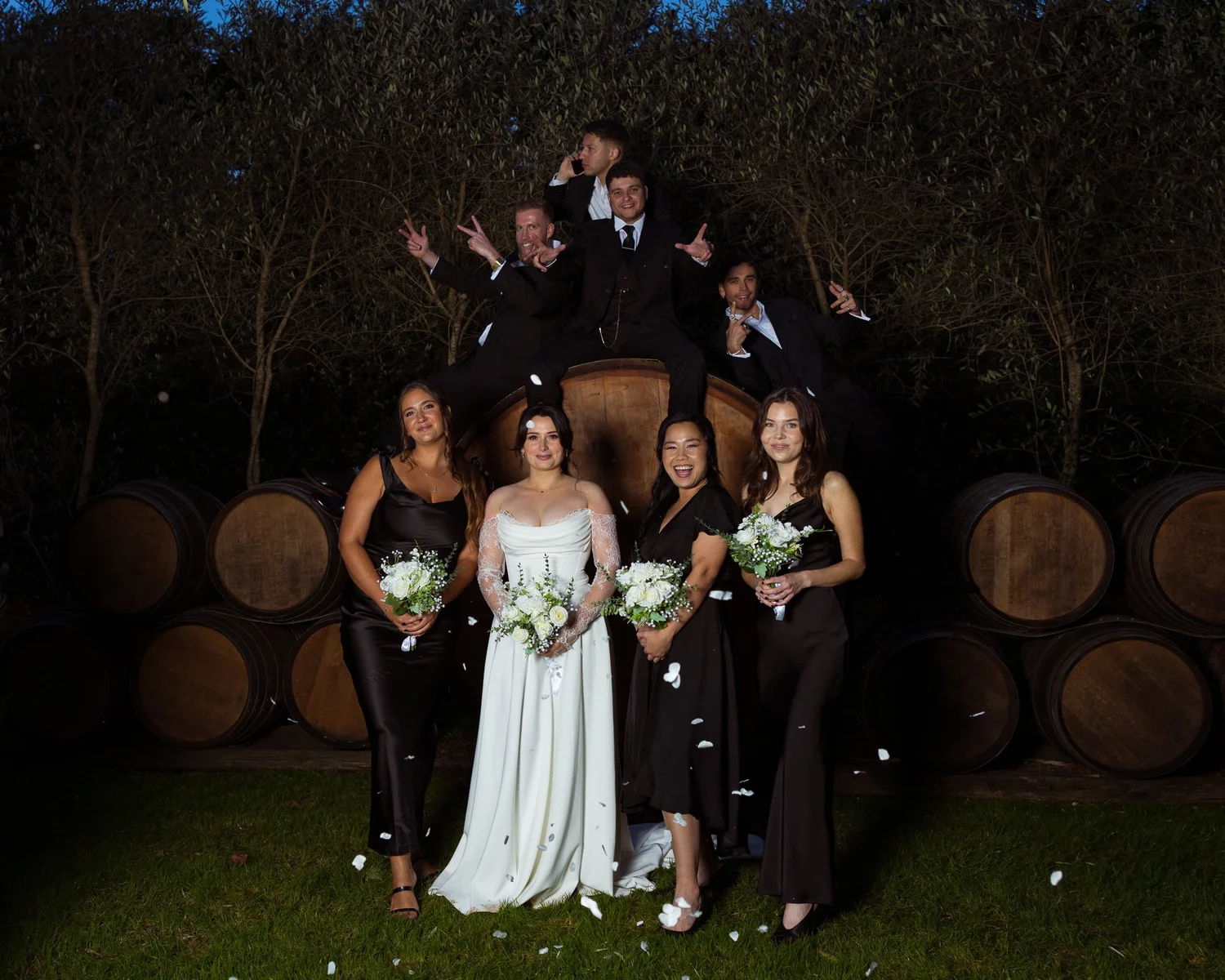 The bridal party celebrates among wine barrels at night