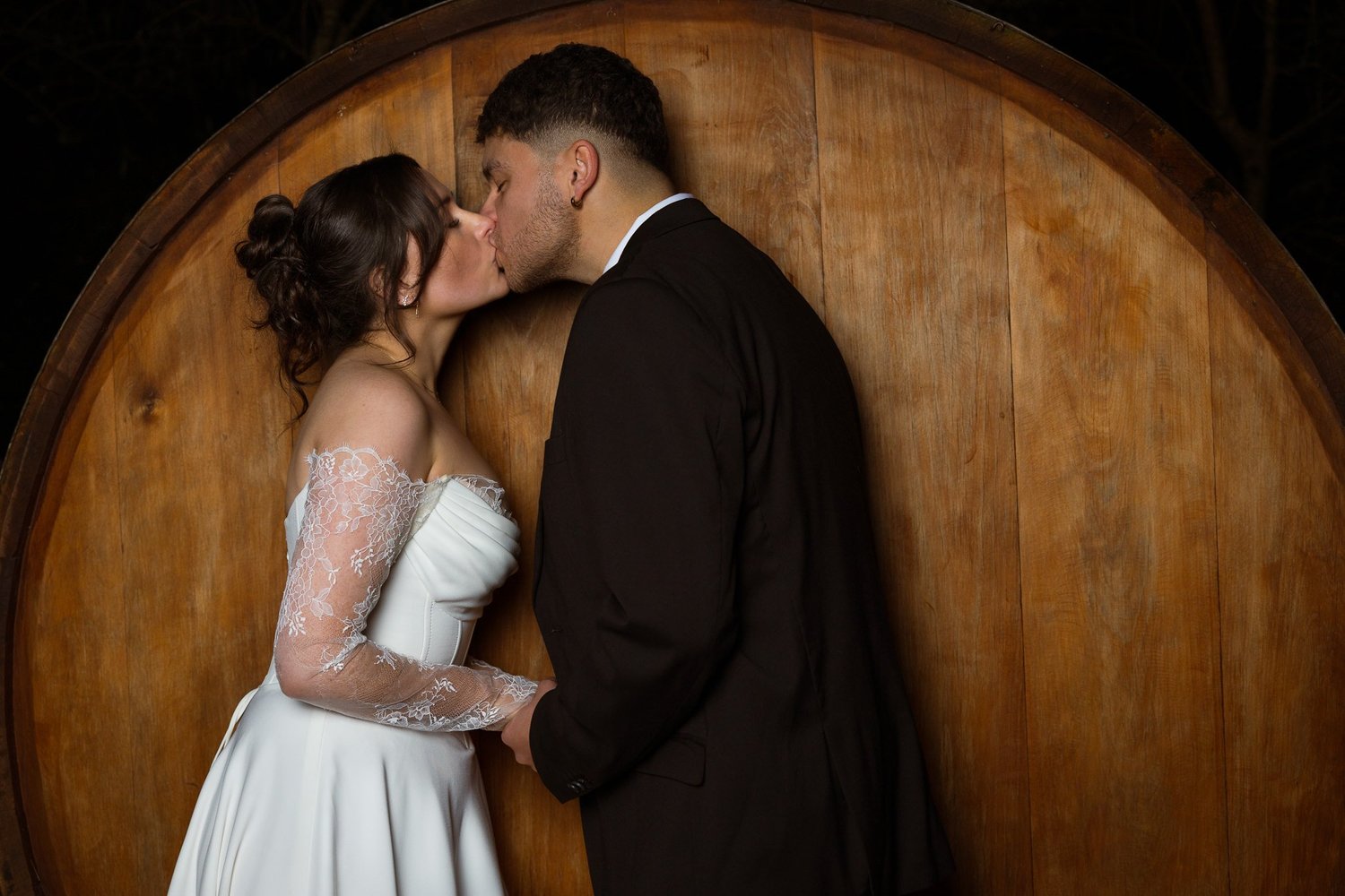 Paige and Connor kiss in front of a large wine barrel