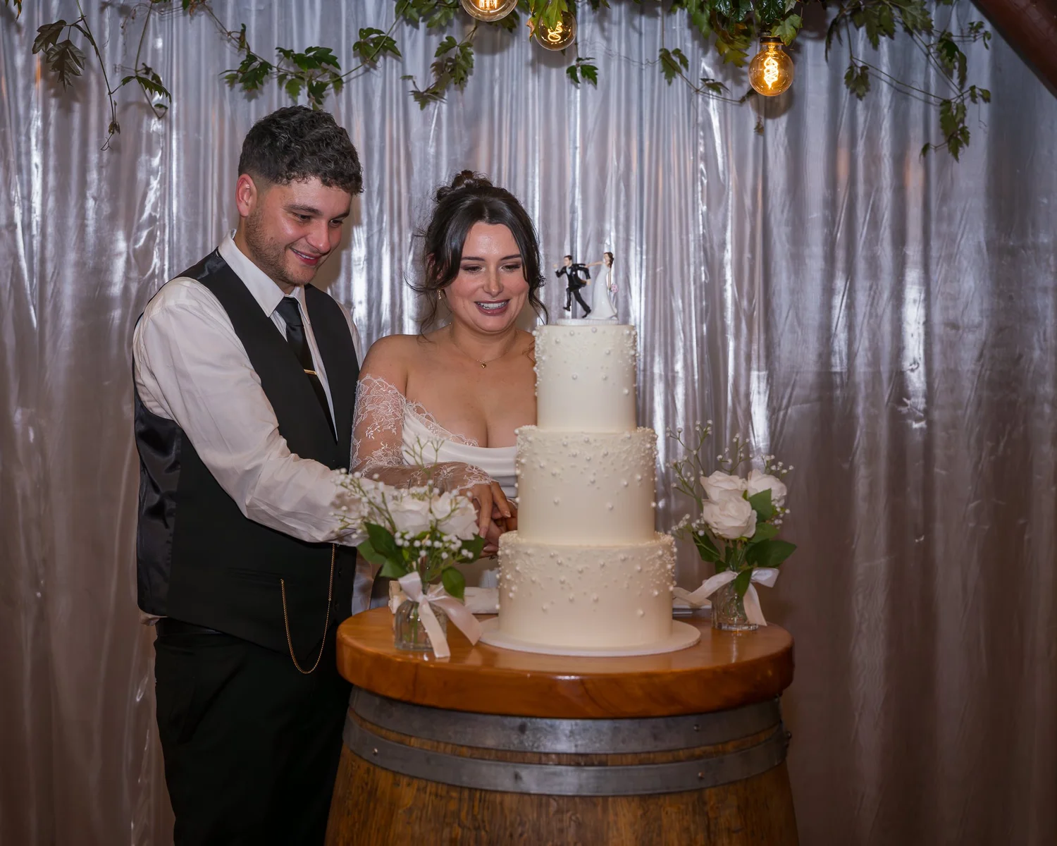 Paige and Connor cut their three-tier cake on a wine barrel