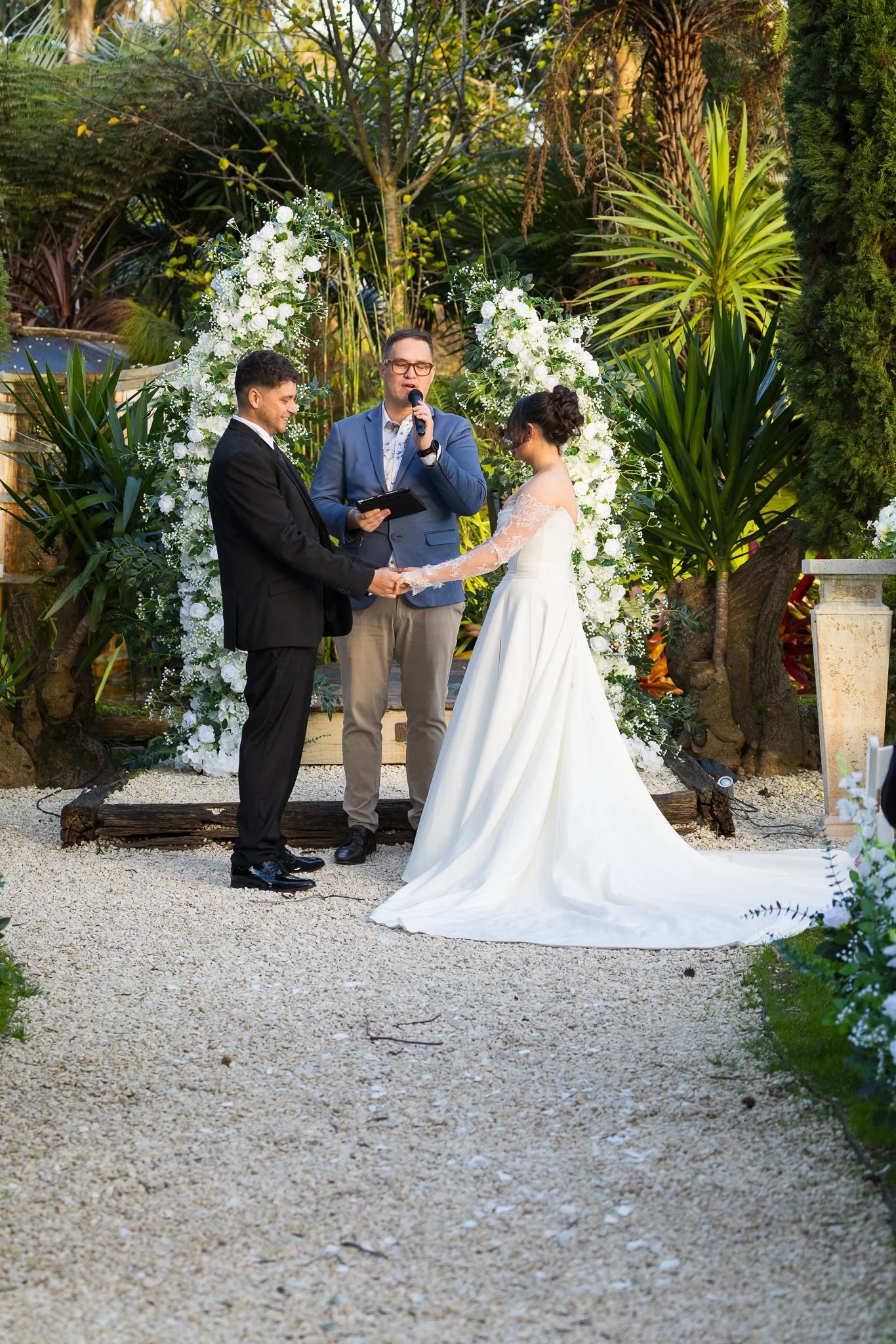 Paige and Connor hold hands under the floral arch during their garden ceremony