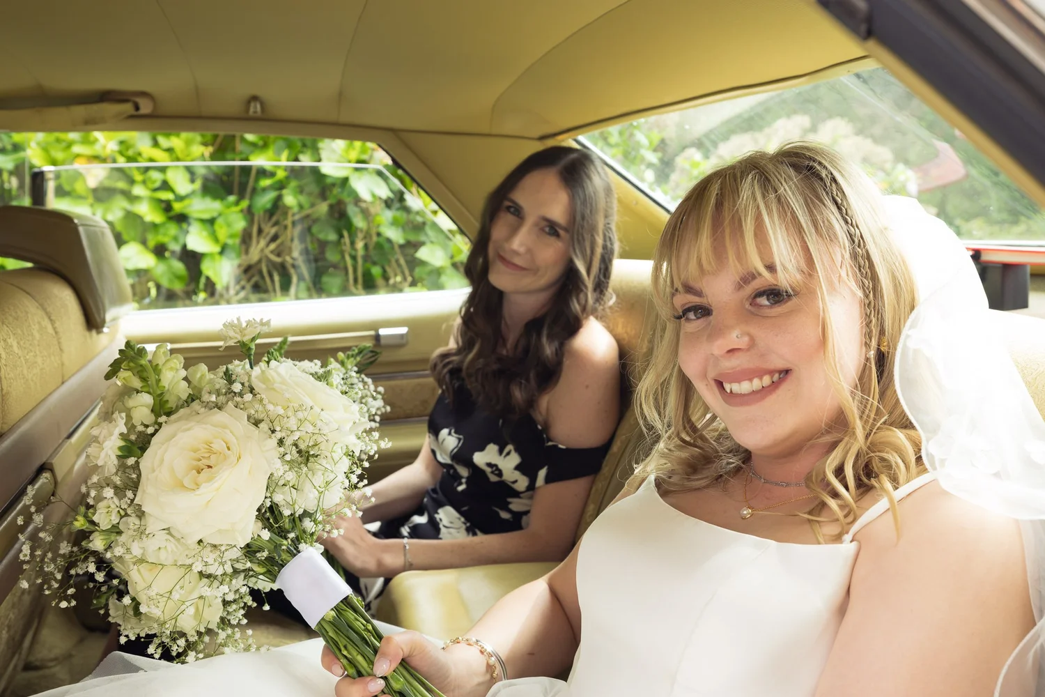 Shannon and a bridesmaid smile from a vintage car