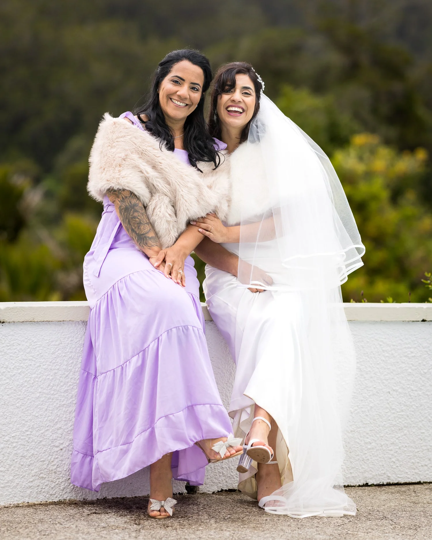 Feby and her bridesmaid sit together on a wall