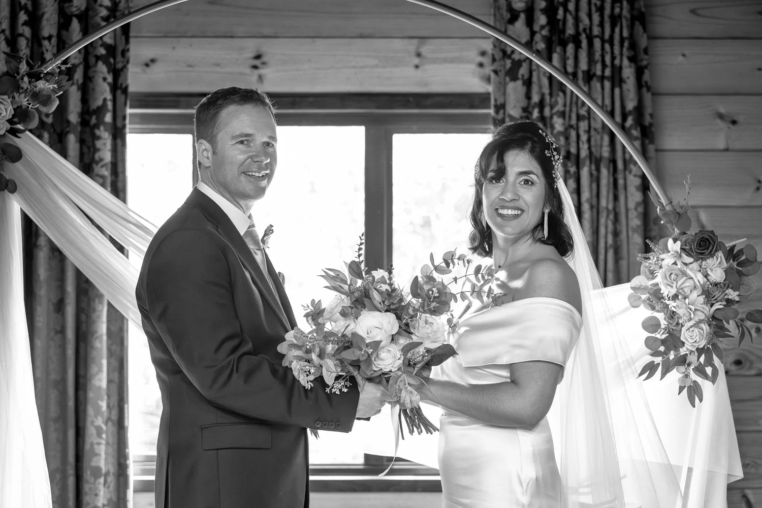 Black and white photo of Feby and Steven under a floral arch