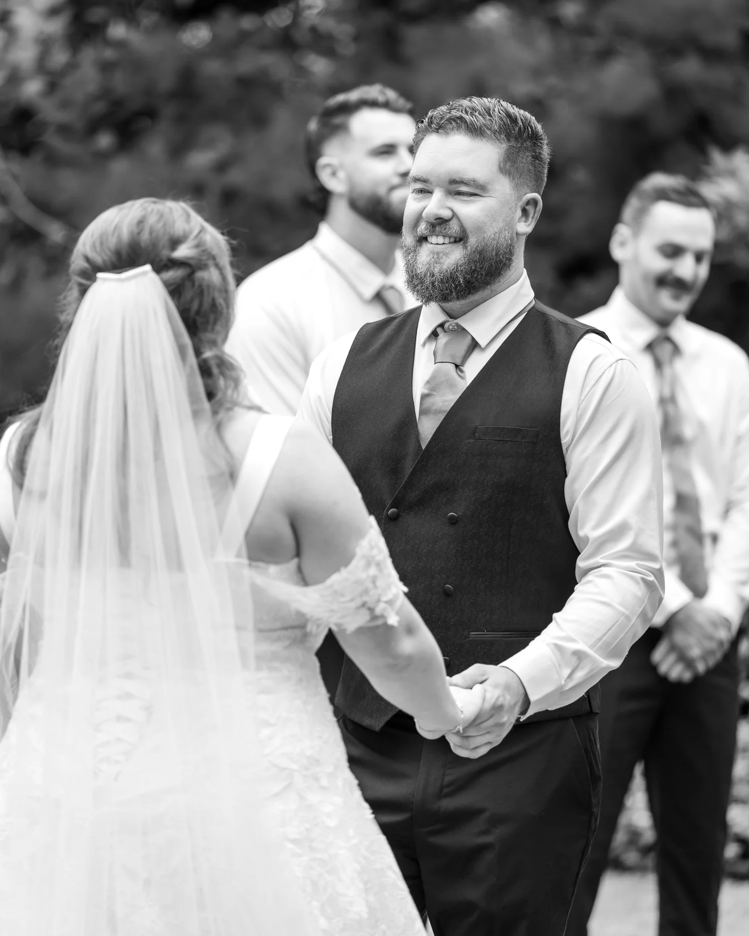 Black and white photo of Kyle laughing as he holds Janine's hands