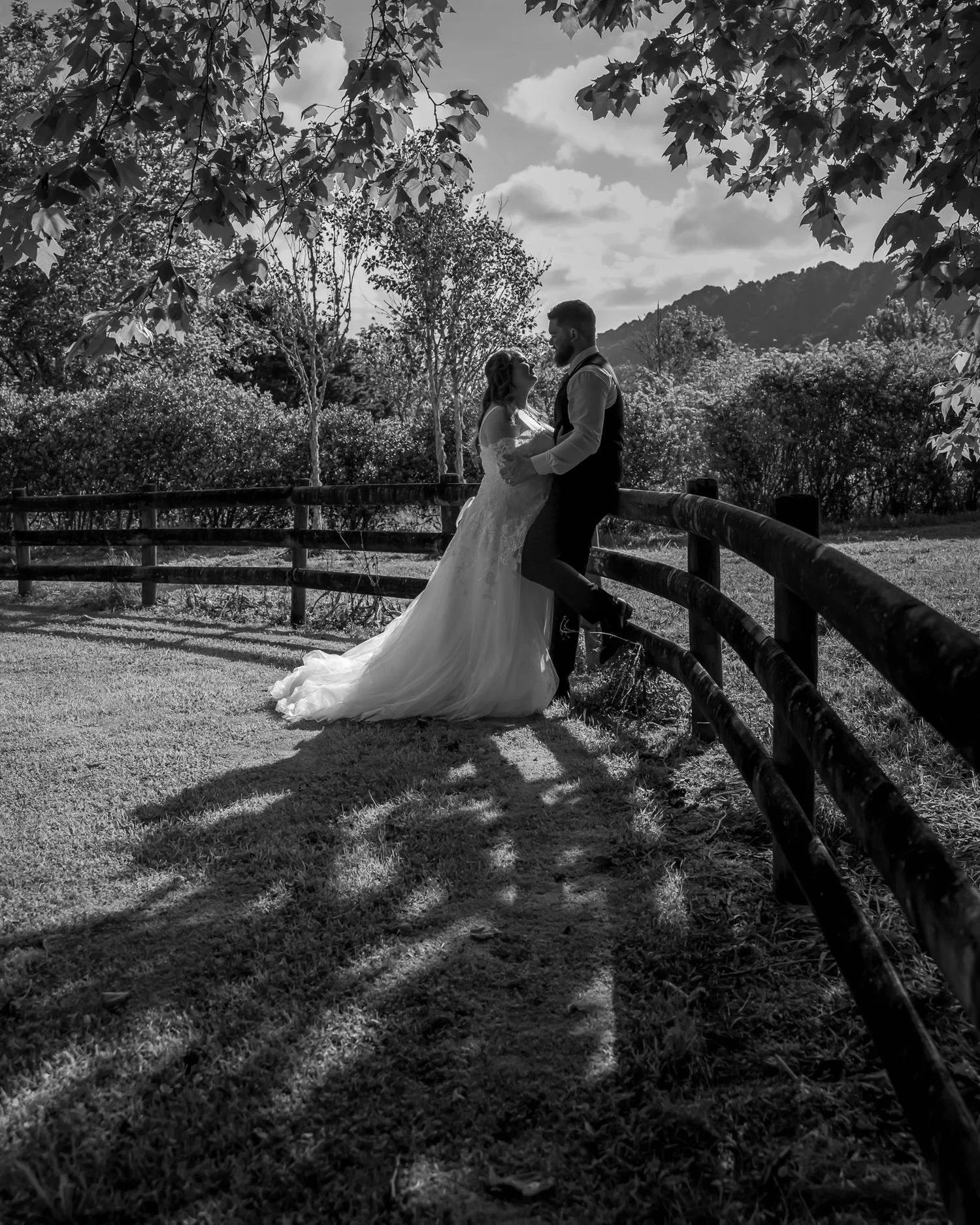 Black and white photo of Janine and Kyle by a fence with hills behind