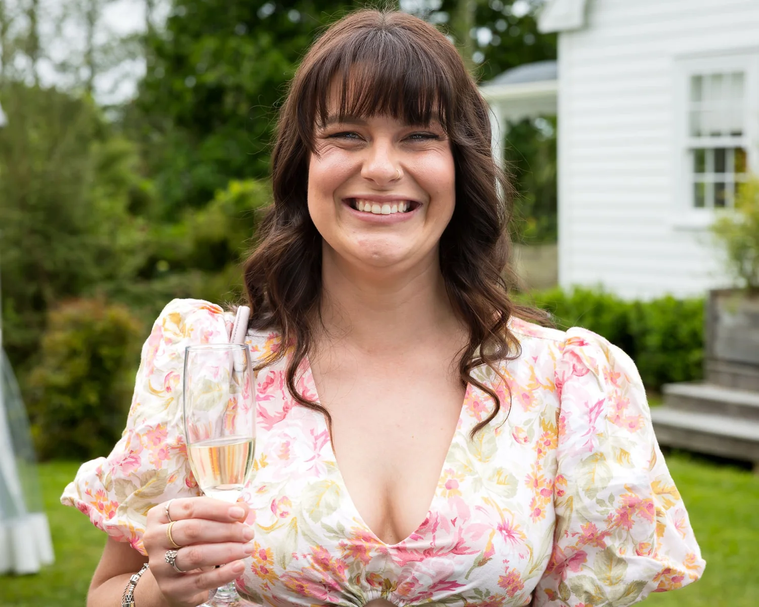 A guest in a floral dress smiles with a glass of wine