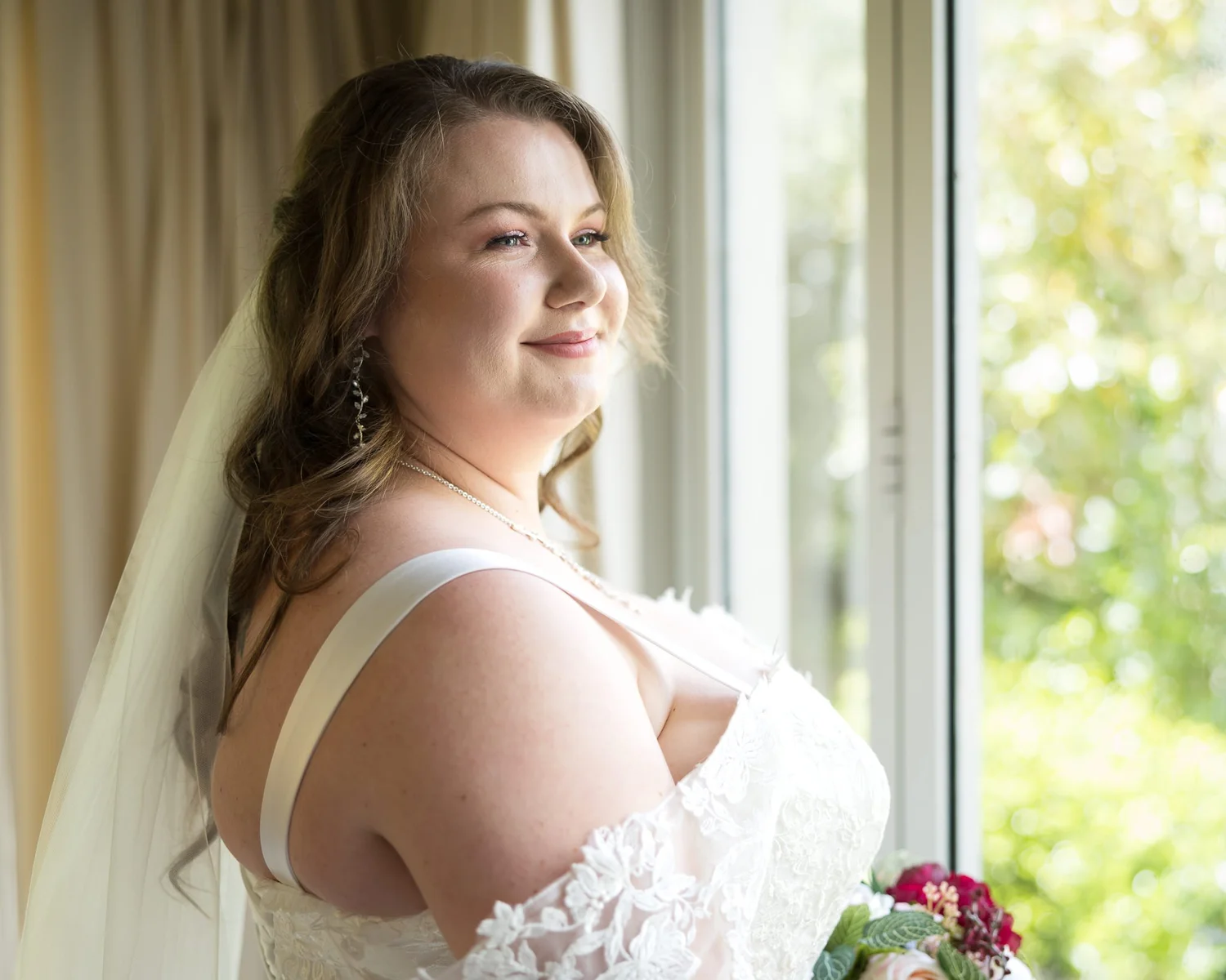 Janine looks out of a window in her gown and veil