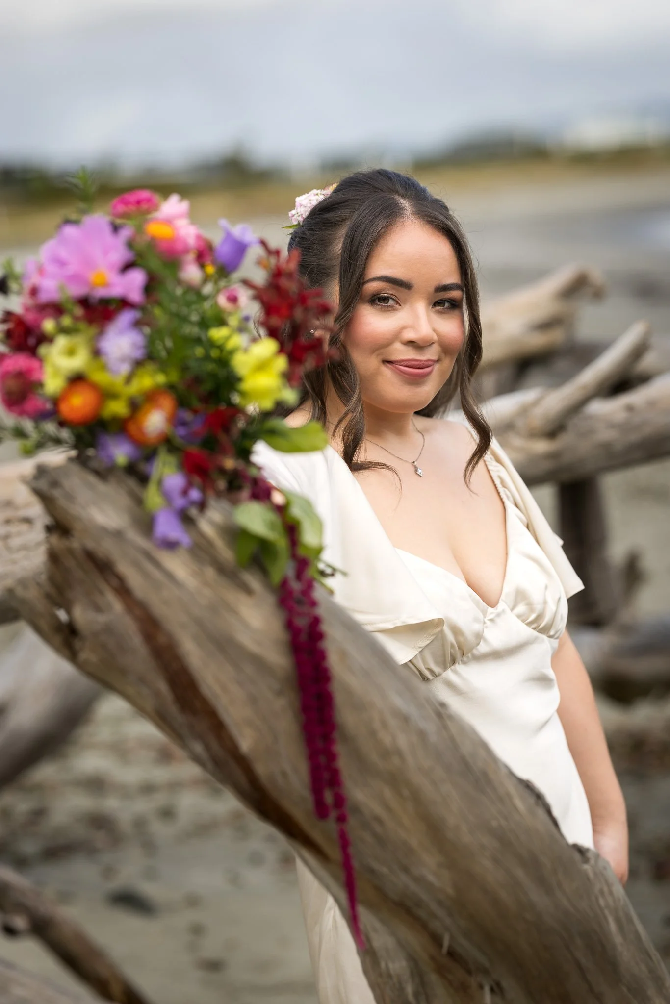 Cerise holds a colourful bouquet against driftwood on the beach