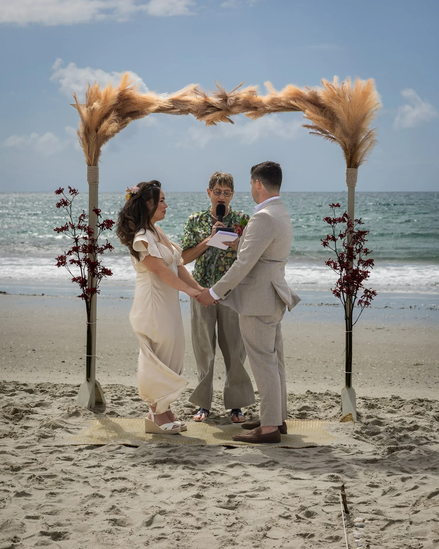 Cerise and Nick exchange vows under a pampas grass arch on the beach