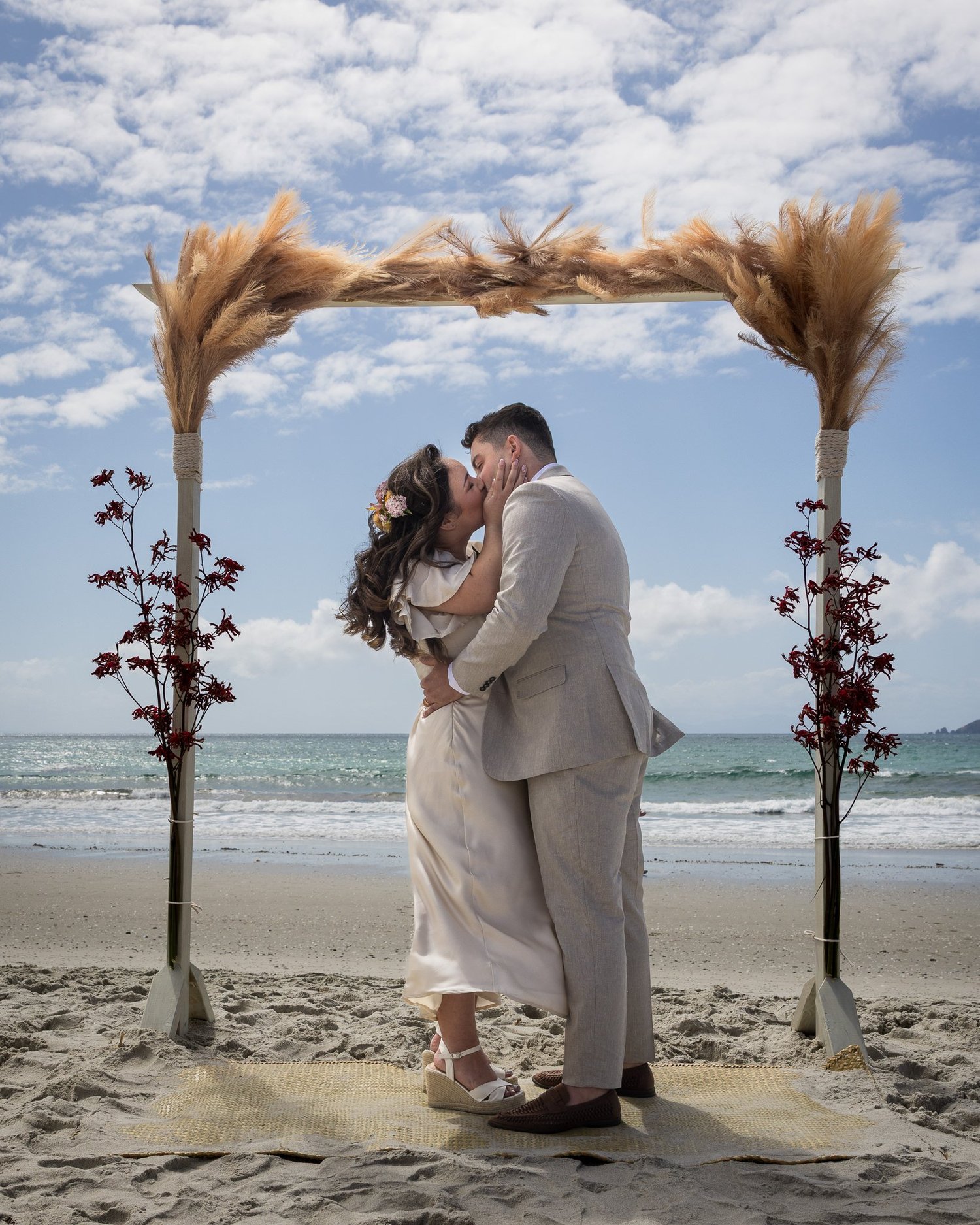 Cerise and Nick kiss under the pampas grass arch by the sea