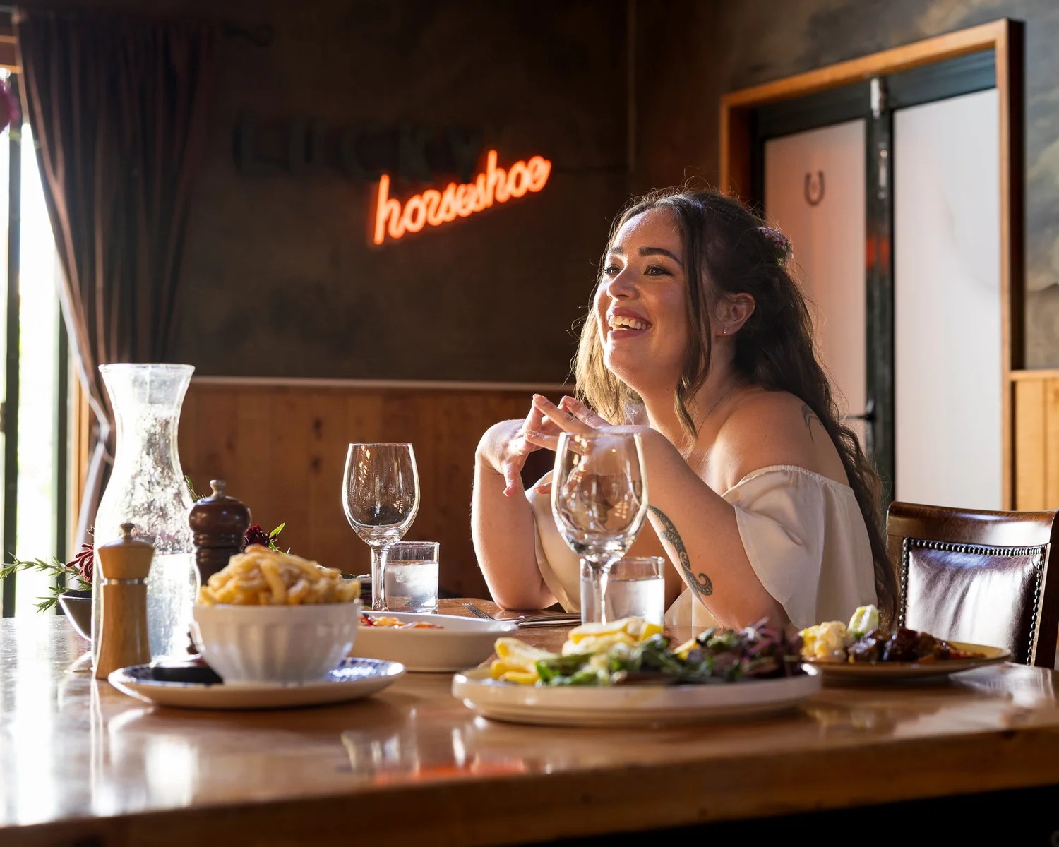 Cerise laughs at the table beneath a neon horseshoe sign