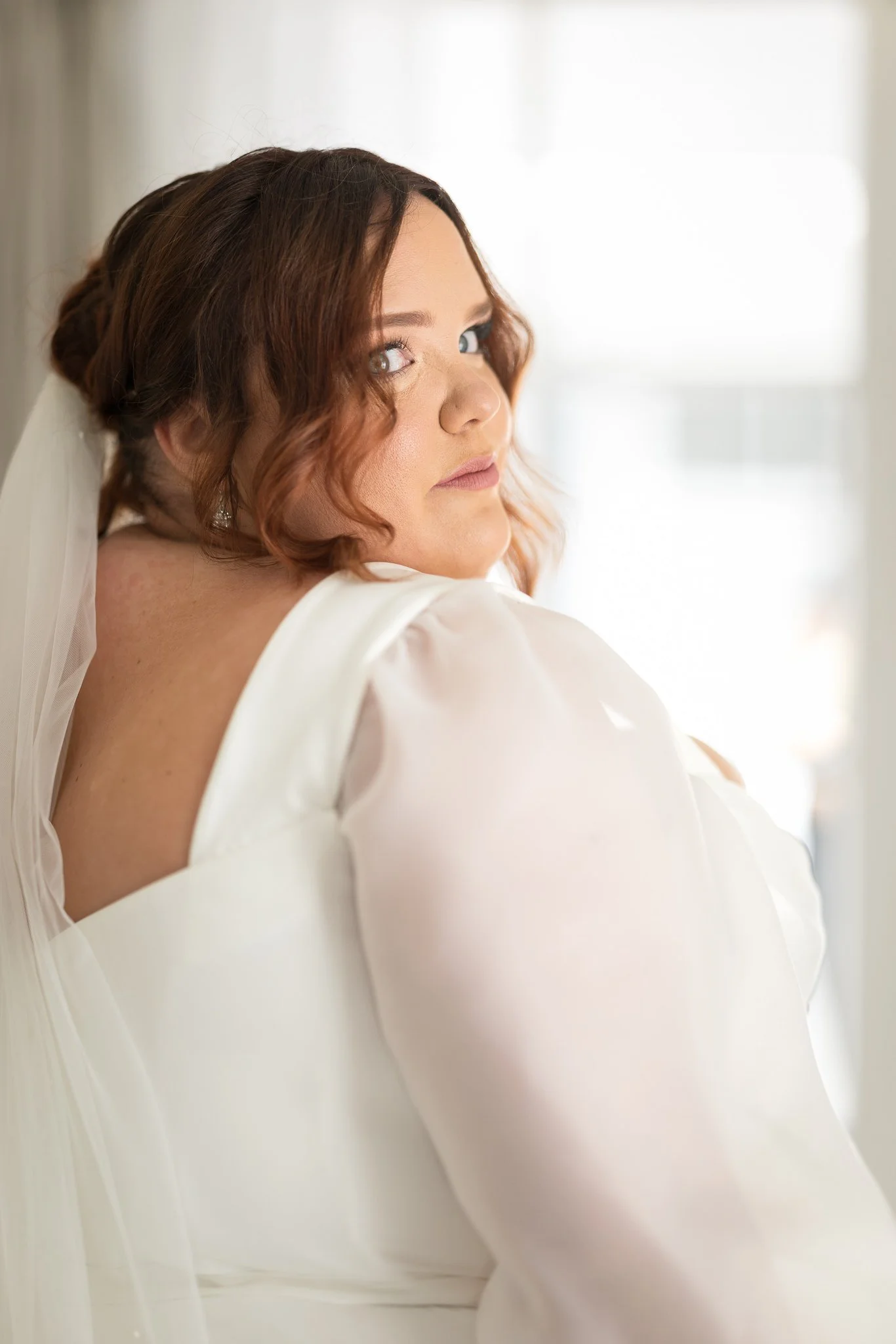 Leah in her gown looking over her shoulder by a window