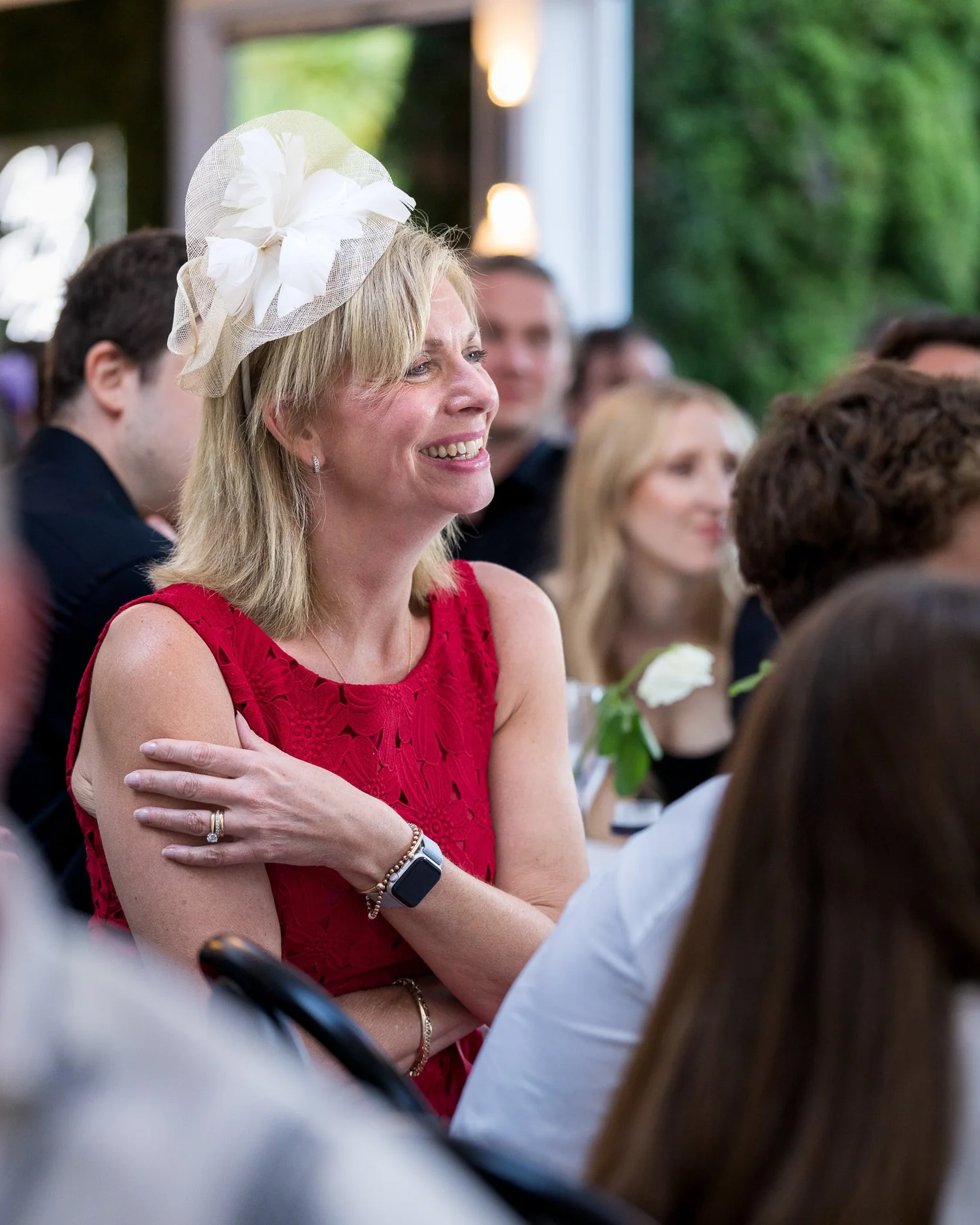 A guest in a red dress and fascinator smiles at the speeches