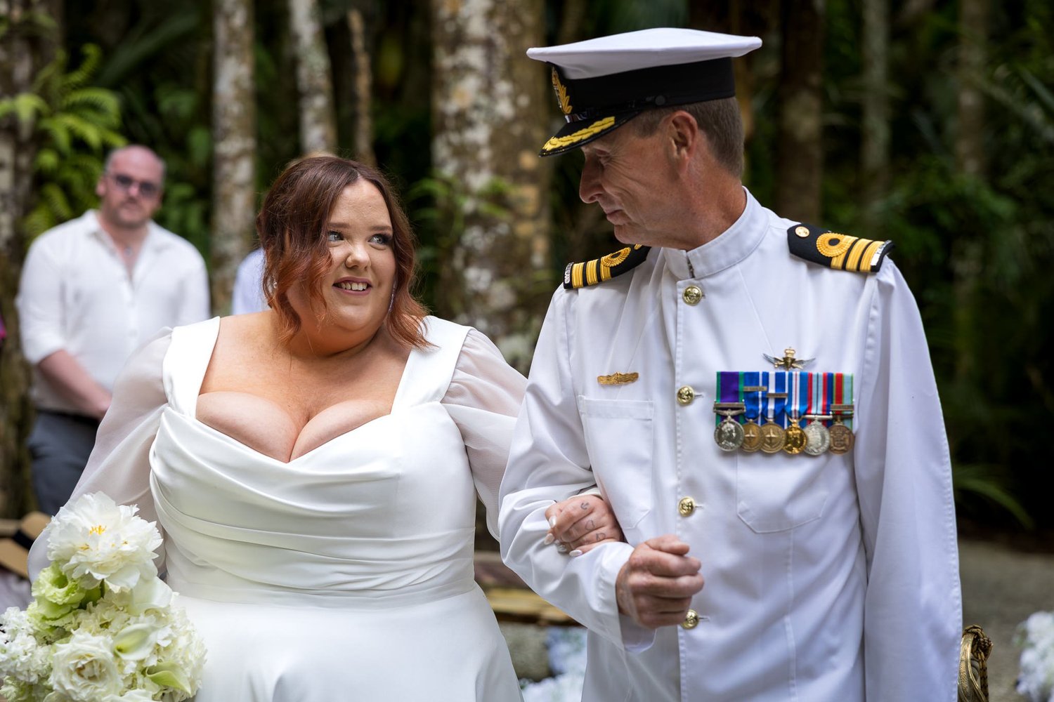 A naval officer in white uniform walks Leah down the aisle