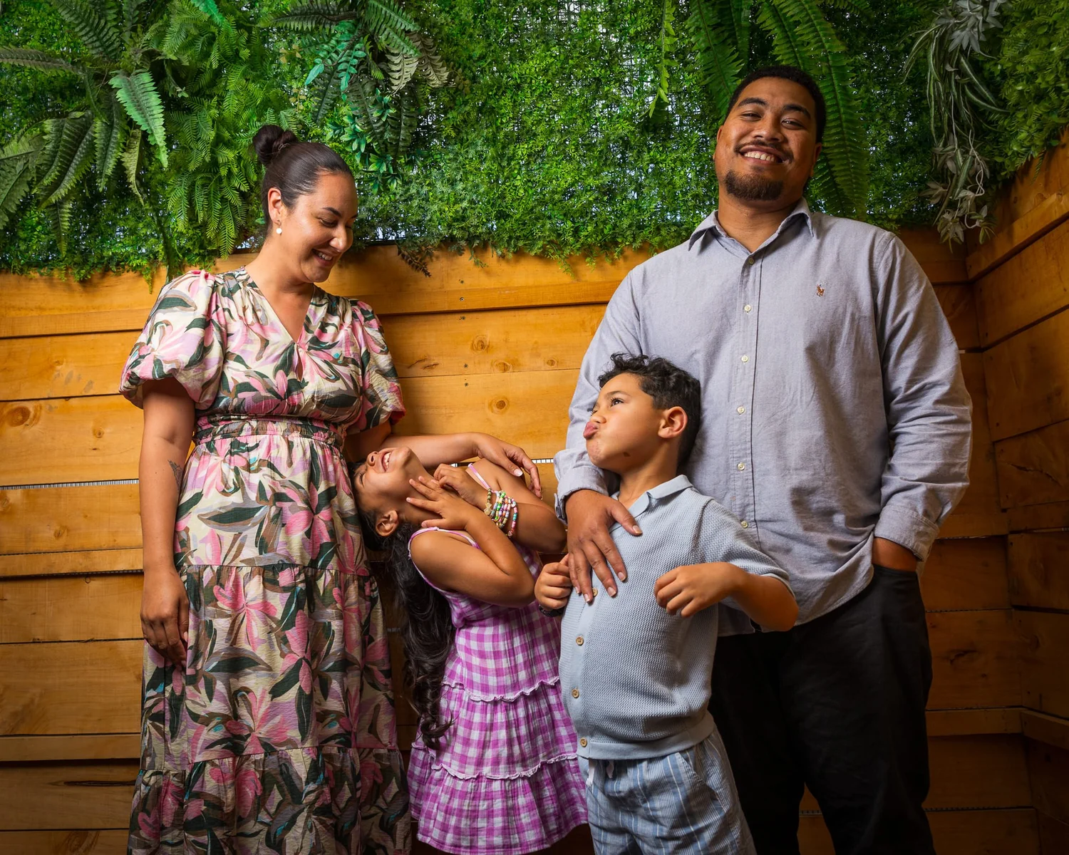 A family laughing together against a timber wall