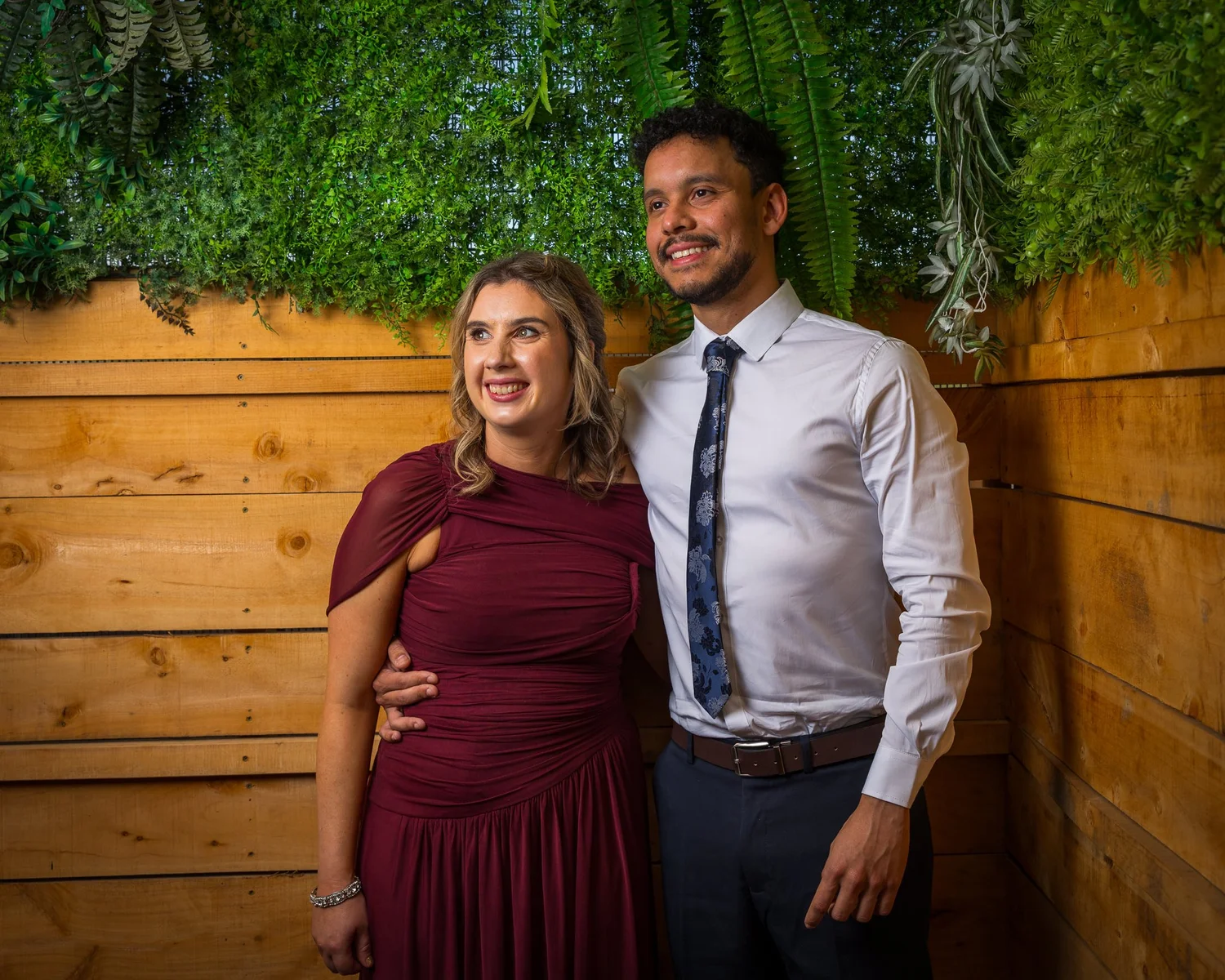 Two guests pose against a timber and greenery backdrop