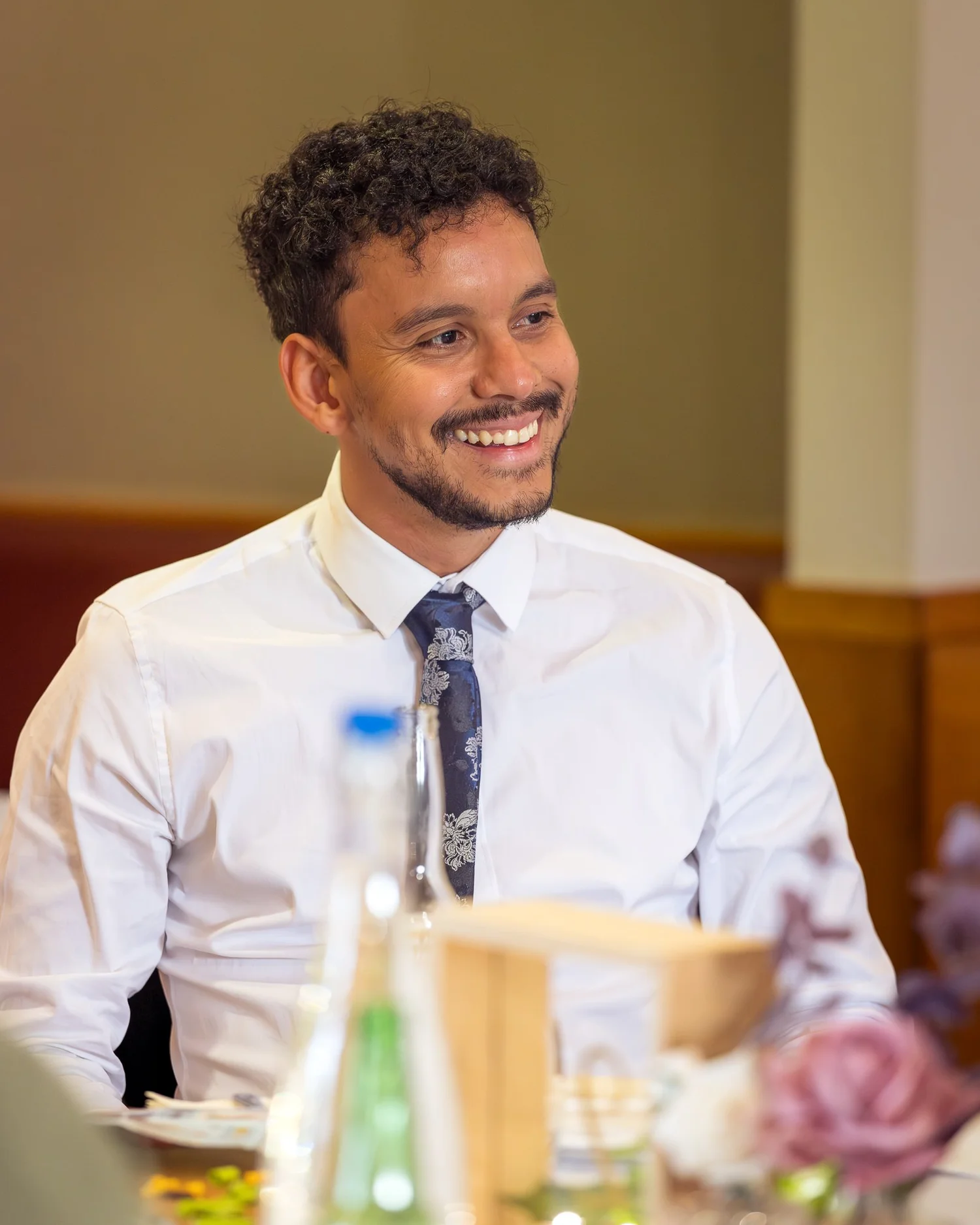 A guest in a shirt and tie laughs at the reception
