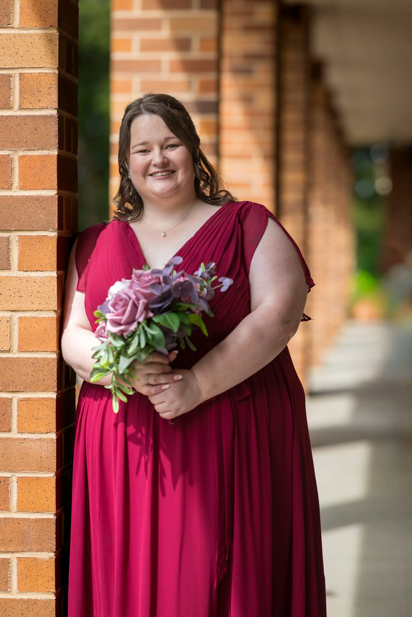 A bridesmaid in red smiles among brick columns