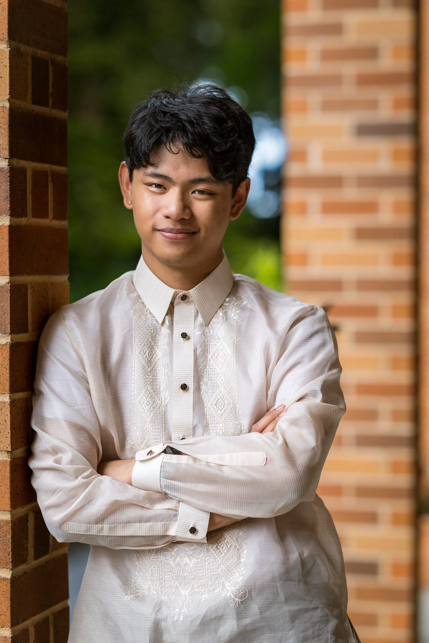 A groomsman in a barong with arms folded beside a brick column
