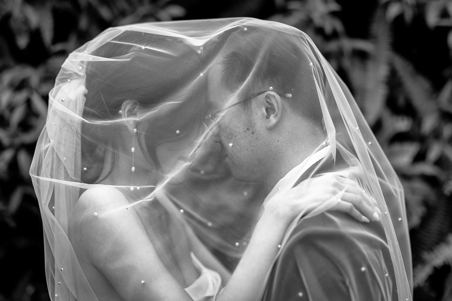Black and white photo of Cherry and Chi kissing beneath her veil