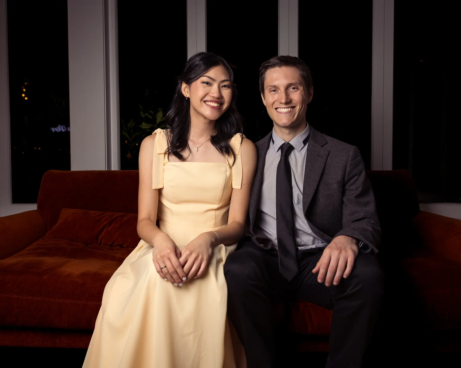 Two guests pose for a portrait on a red velvet sofa