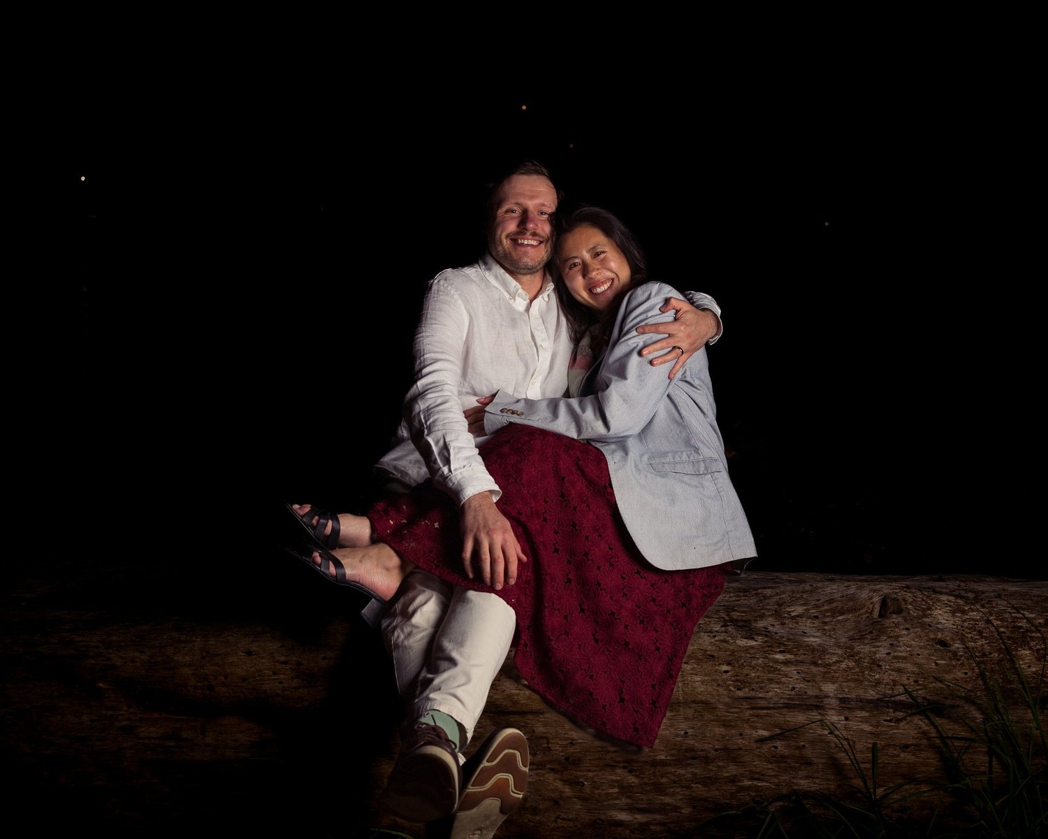 Two guests sit together laughing on a stone wall at night