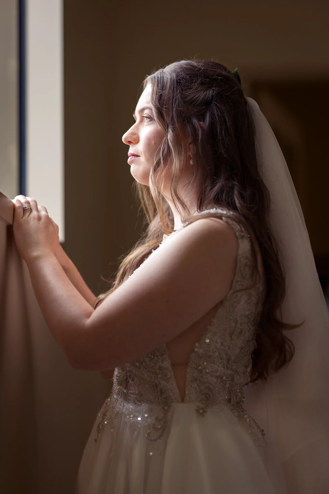 Mikaela by a window in her lace gown and veil