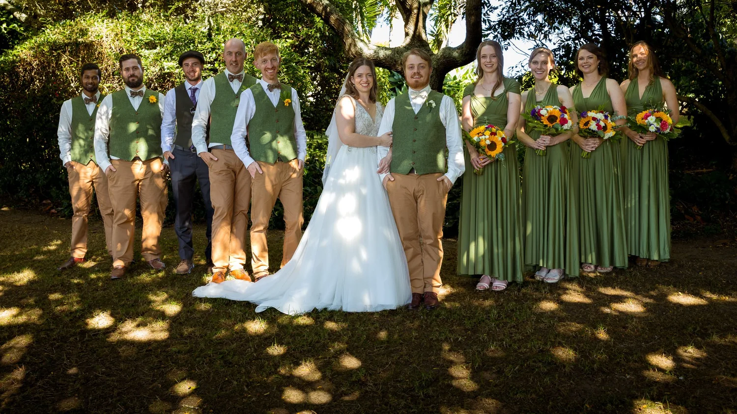 Mikaela and Dylan with their bridal party in green under the trees