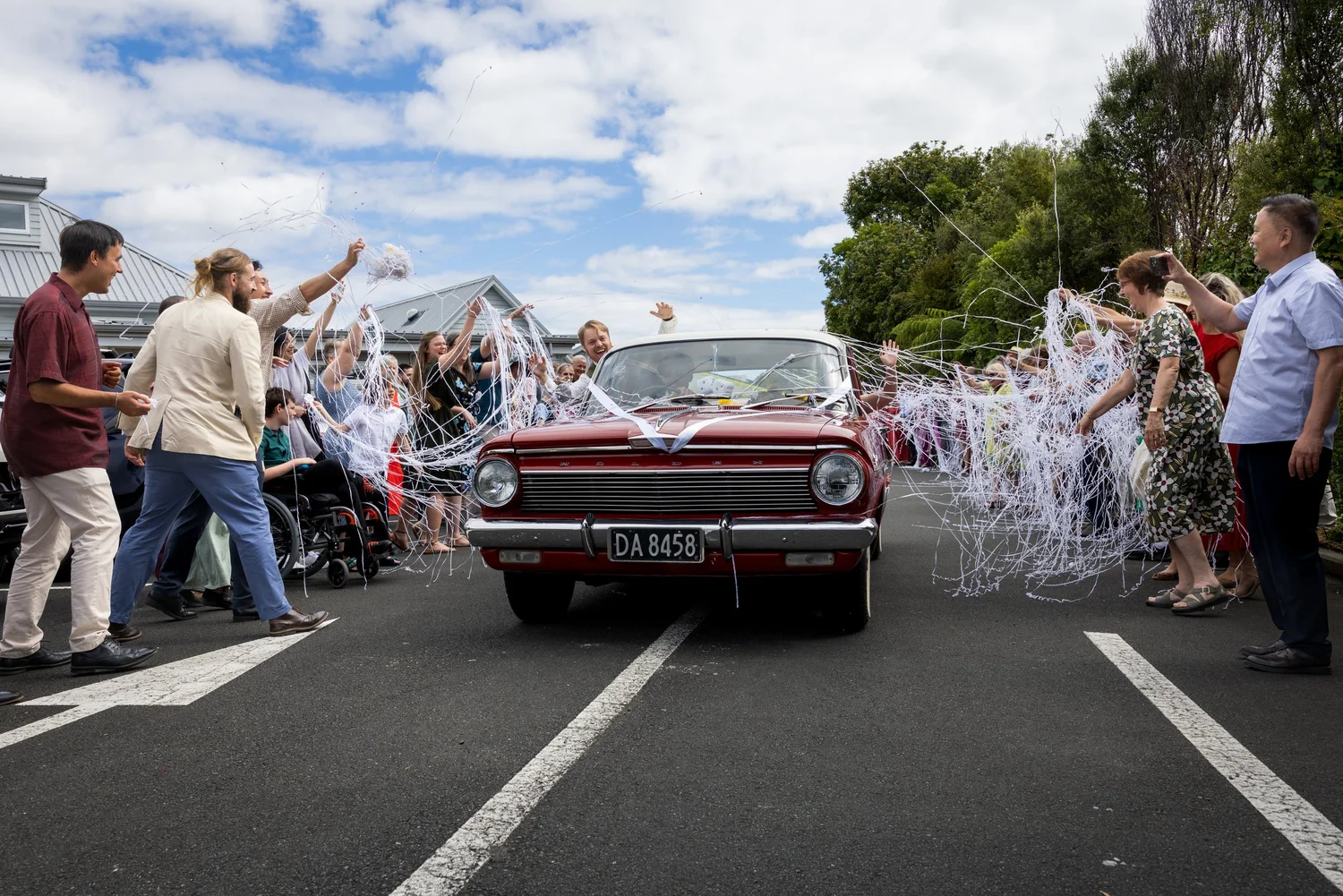 Guests wave streamers as a vintage car drives off