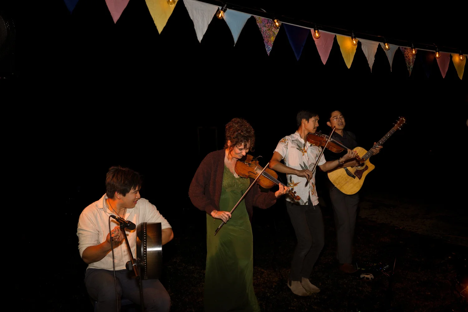 Musicians play fiddle and guitar under festoon bunting