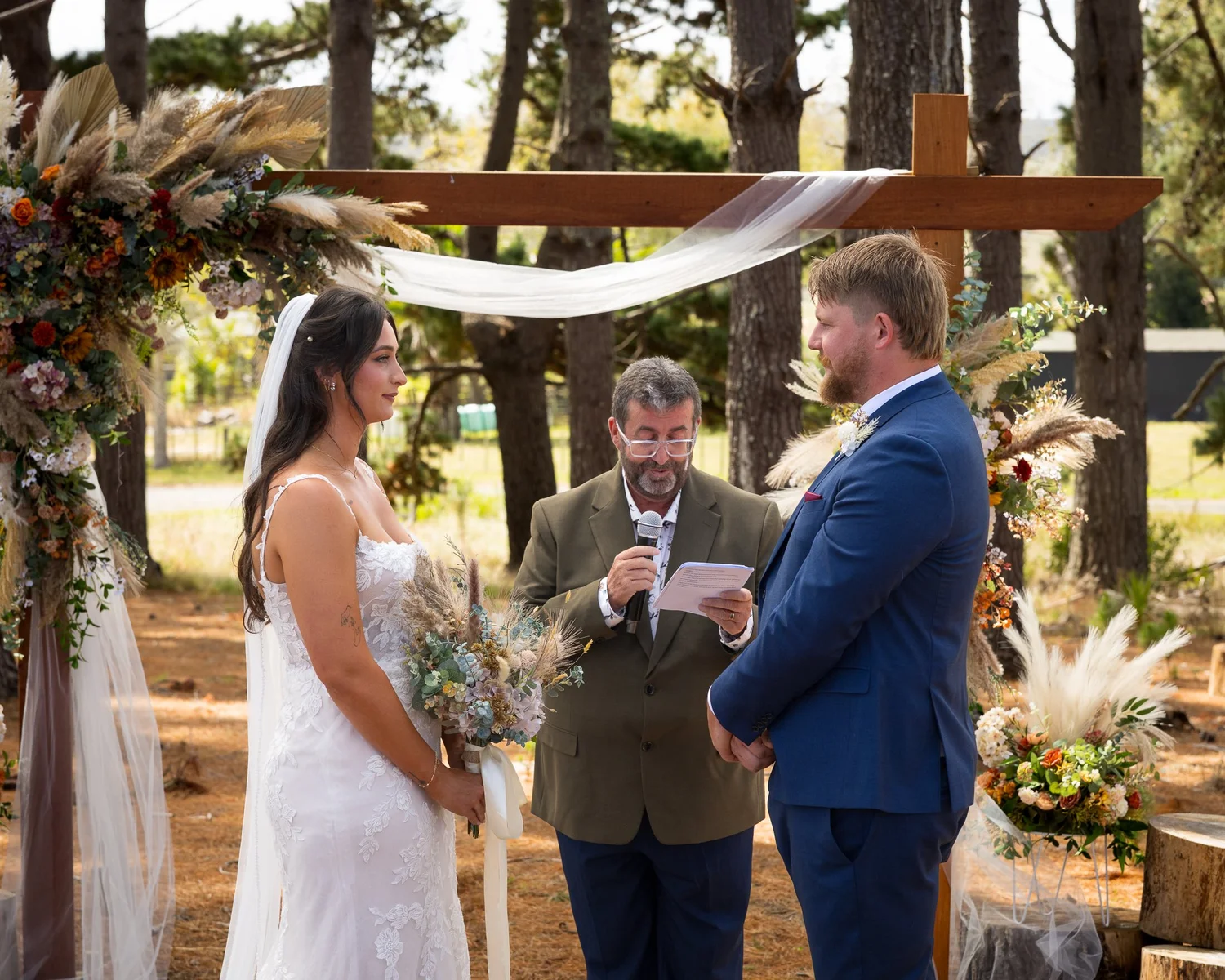 Tay and Jesse with the celebrant under a wooden arch