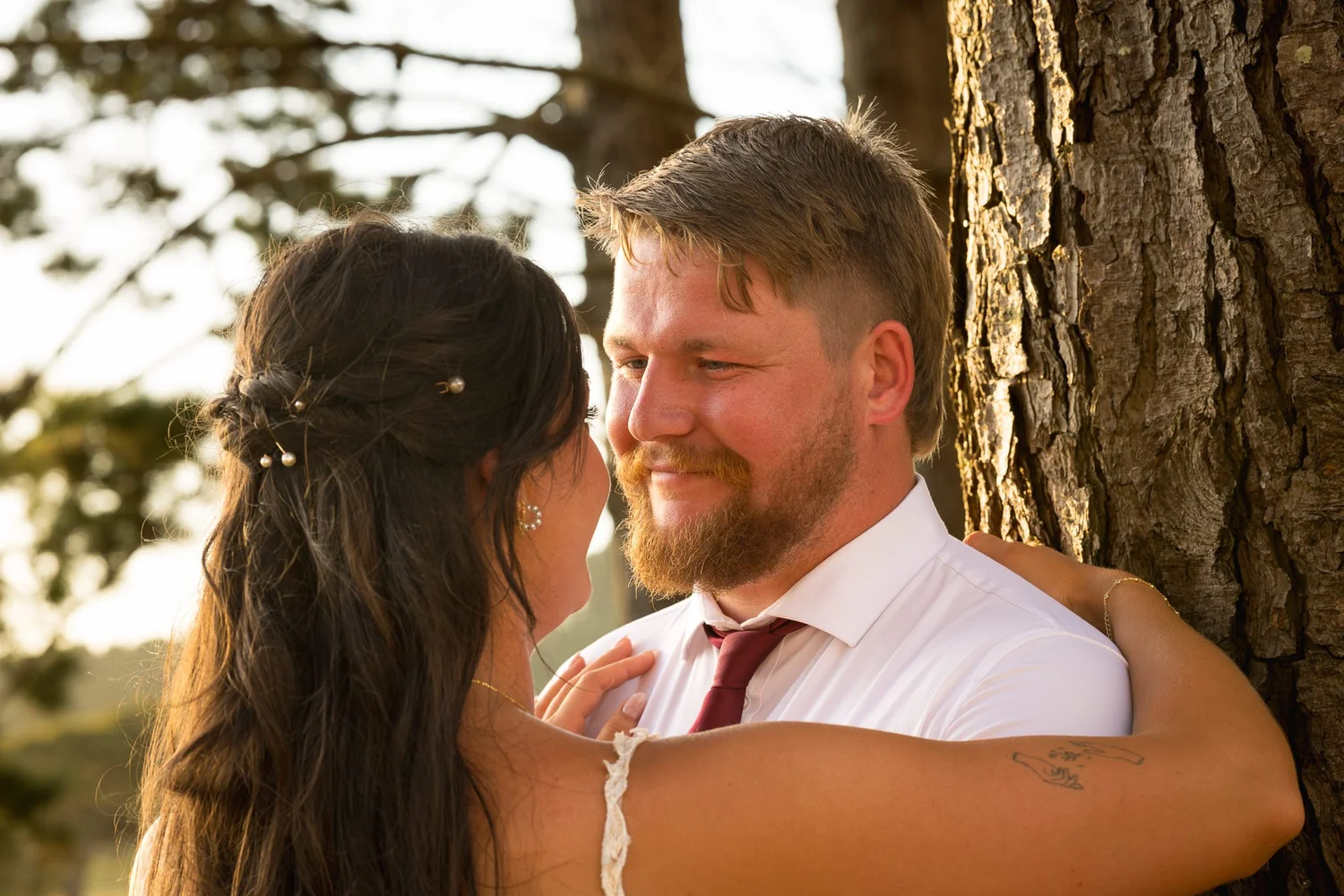 Tay and Jesse smile at each other against a tree