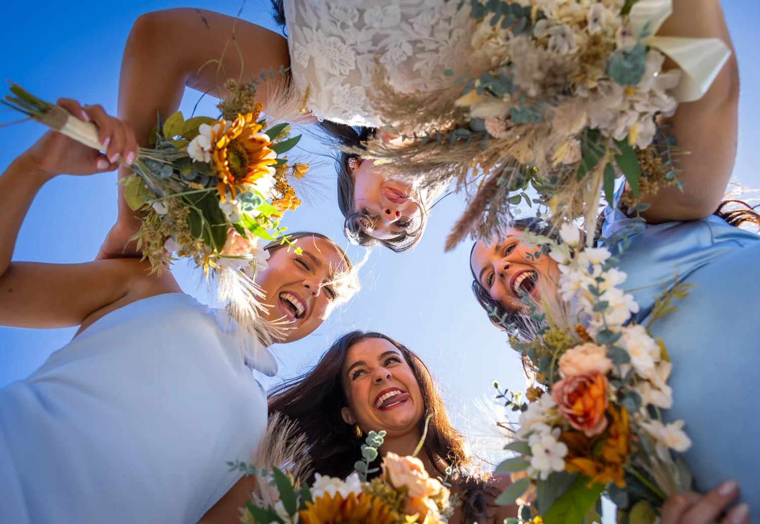 The bridal party looks down into the camera with bouquets