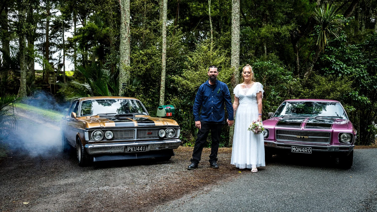 Julia and Alistair between two classic cars as one spins its wheels