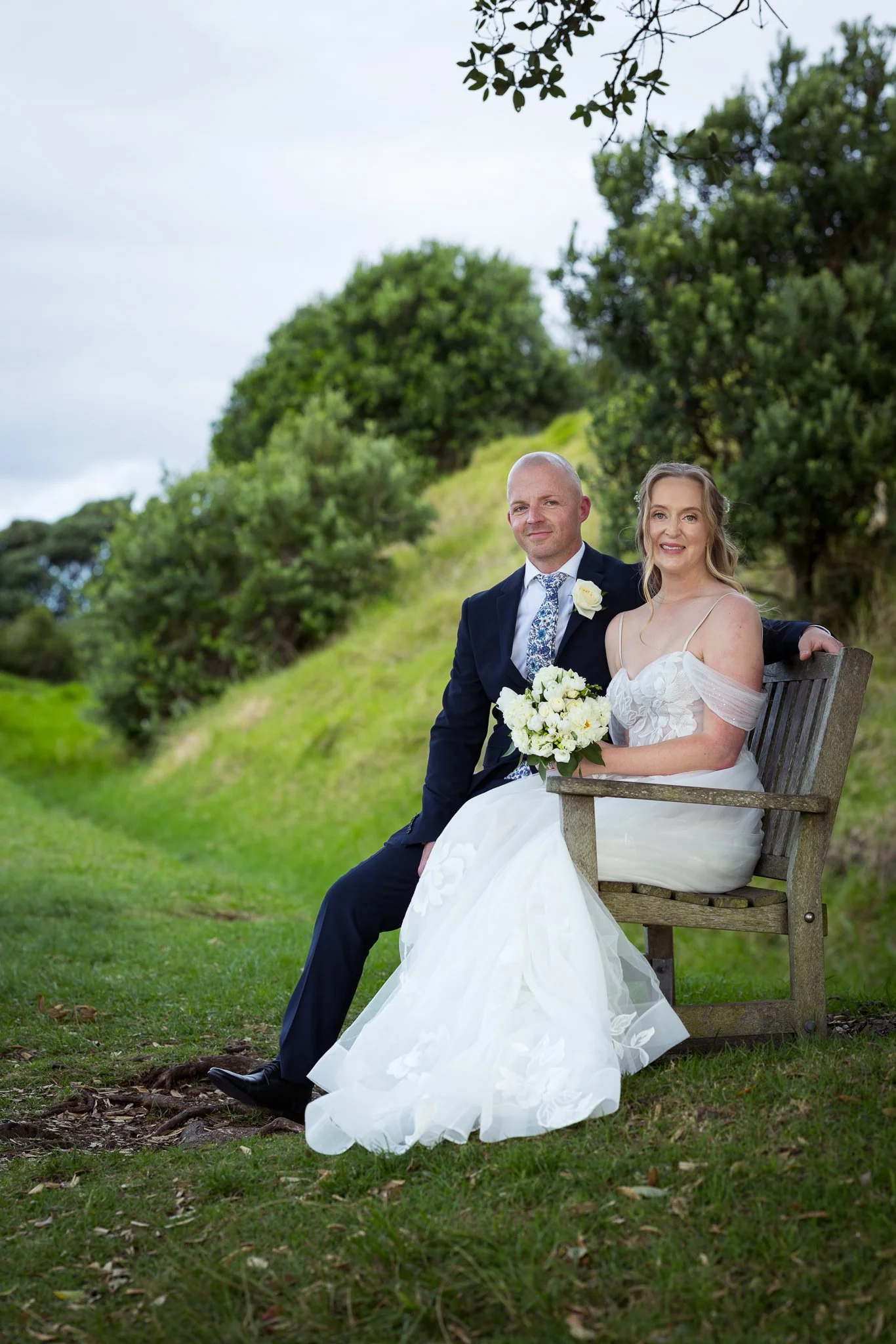 Kayla and Scott sit on a bench on a grassy hill in Devonport