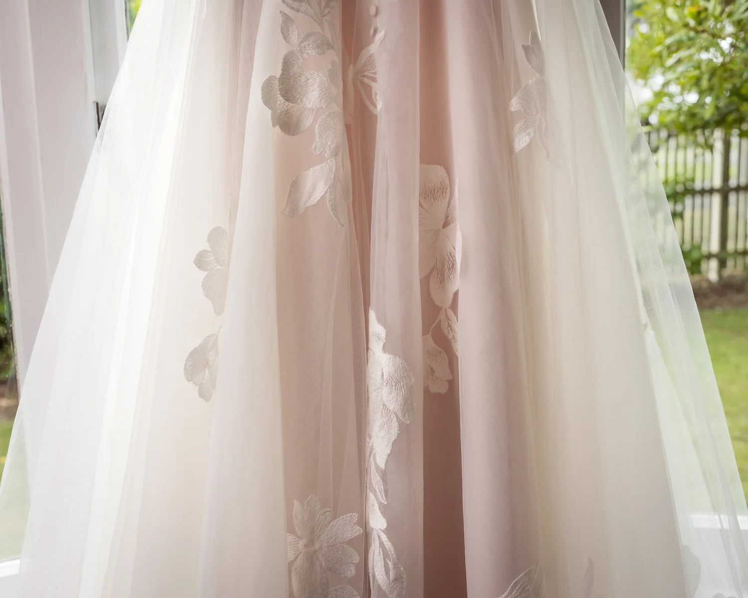 The floral appliqué skirt of Kayla's gown hanging by a window