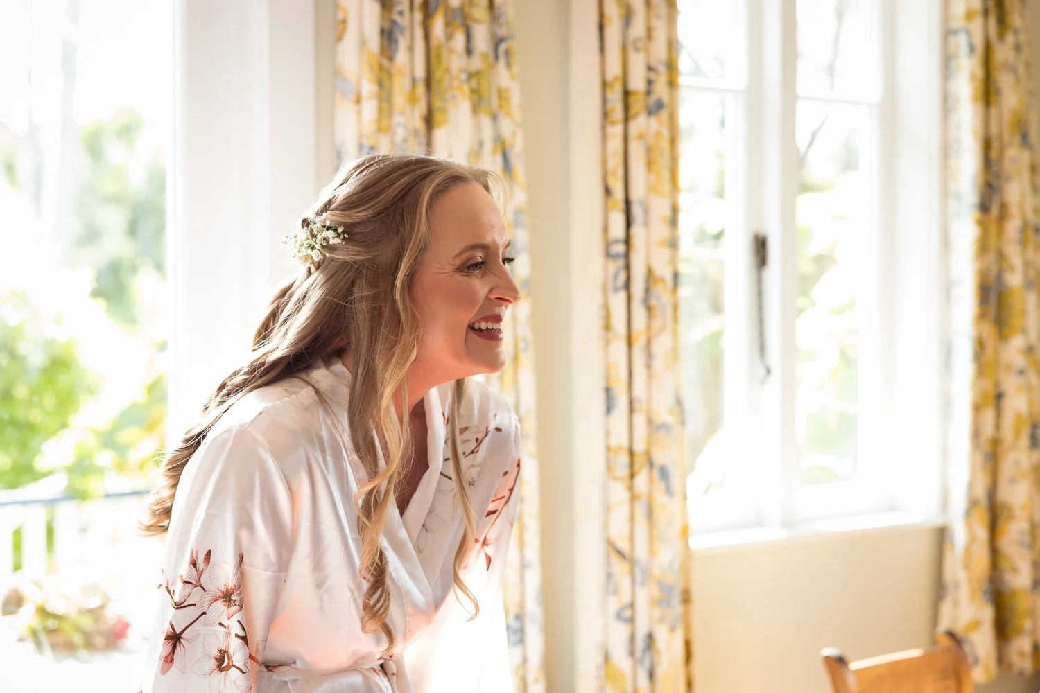Kayla laughs by a window in her floral robe