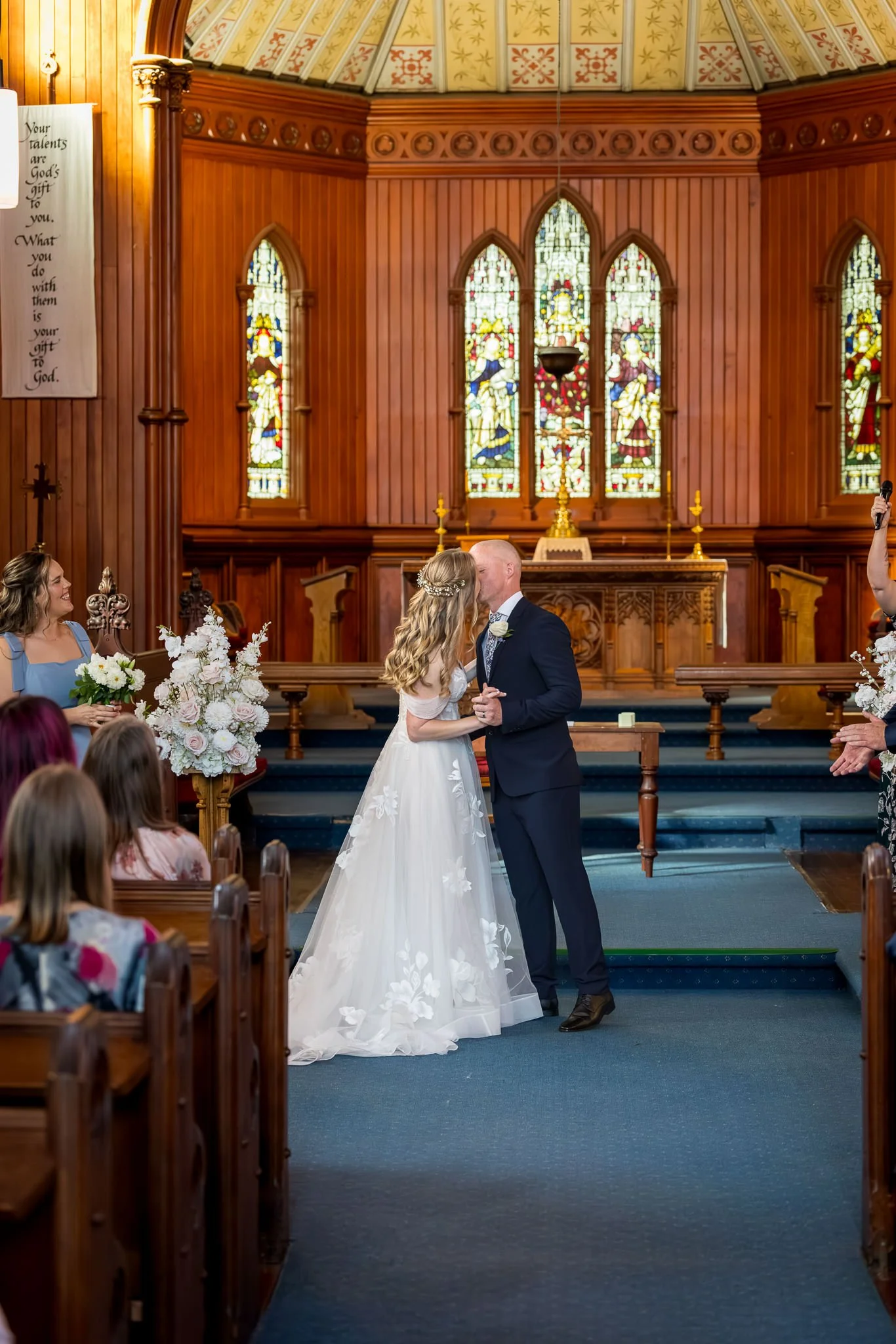 Kayla and Scott kiss at the altar beneath stained-glass windows