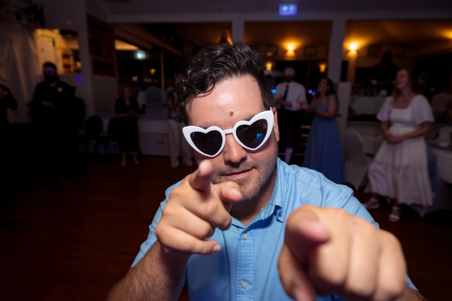 A guest in heart-shaped sunglasses points at the camera