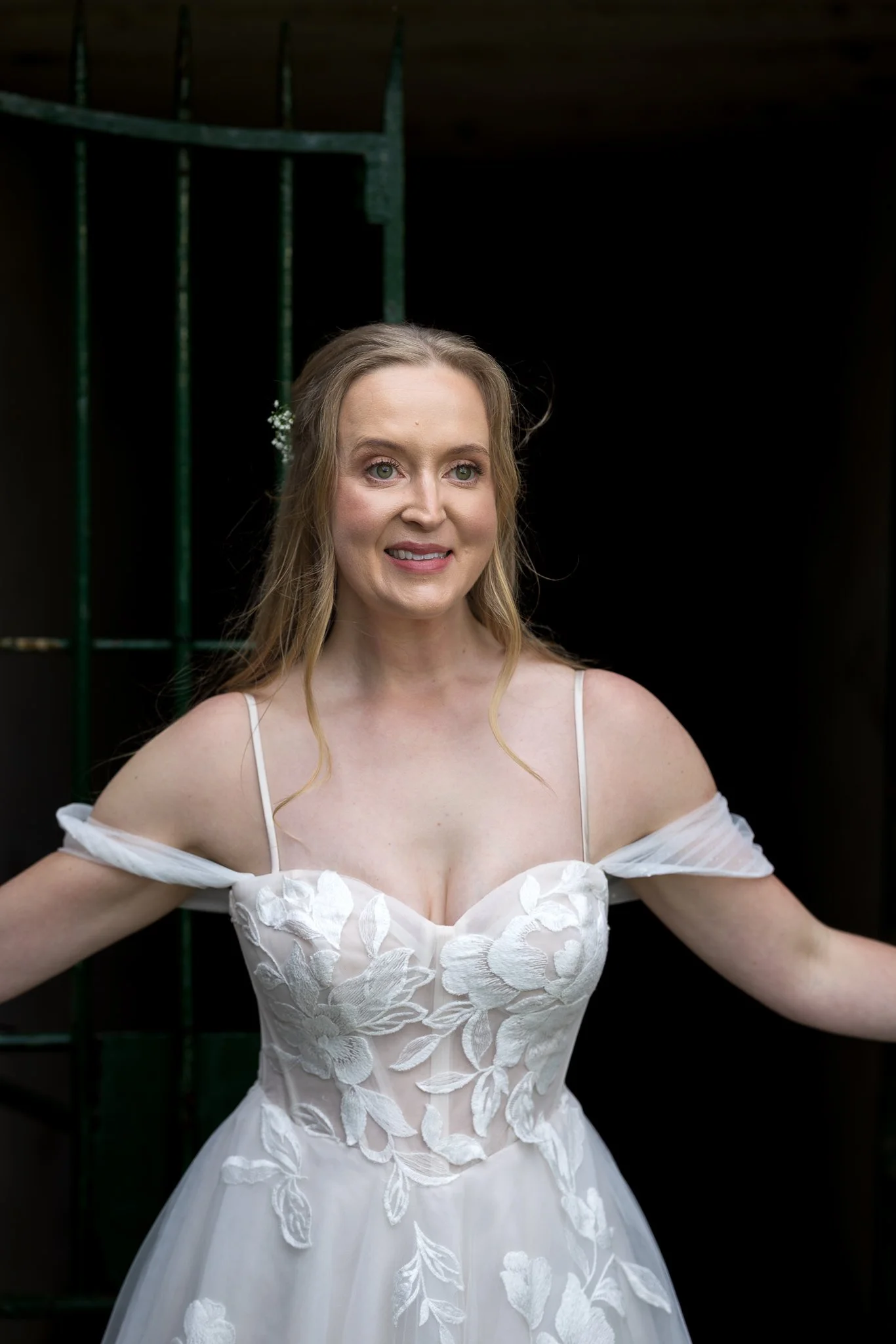 Kayla stands in a dark doorway in her off-the-shoulder gown