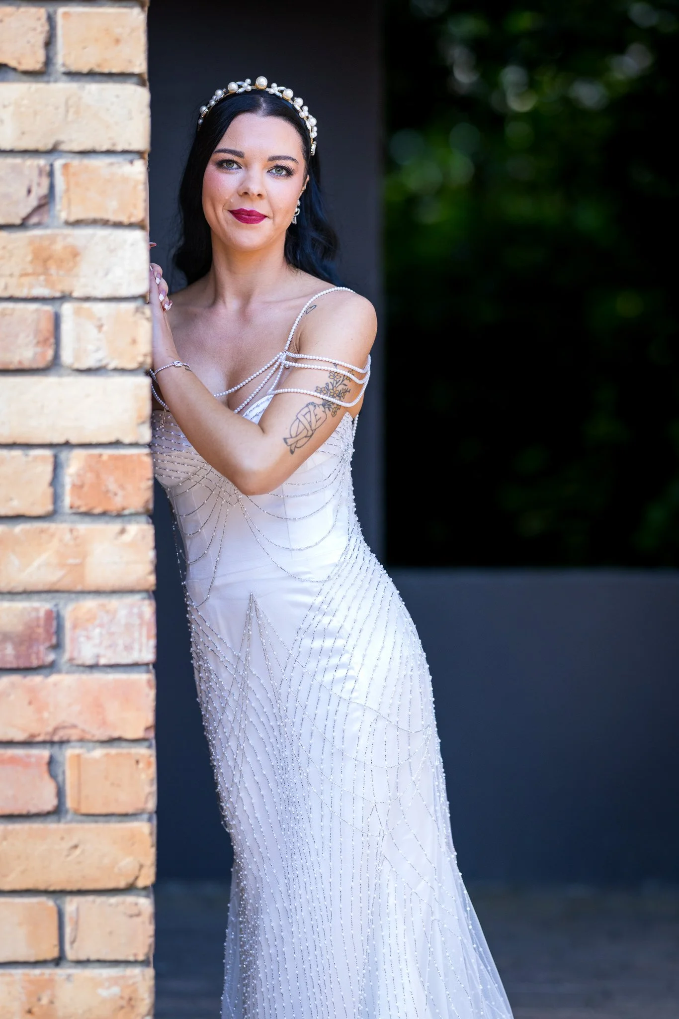 Emma leans against a brick column in her beaded gown