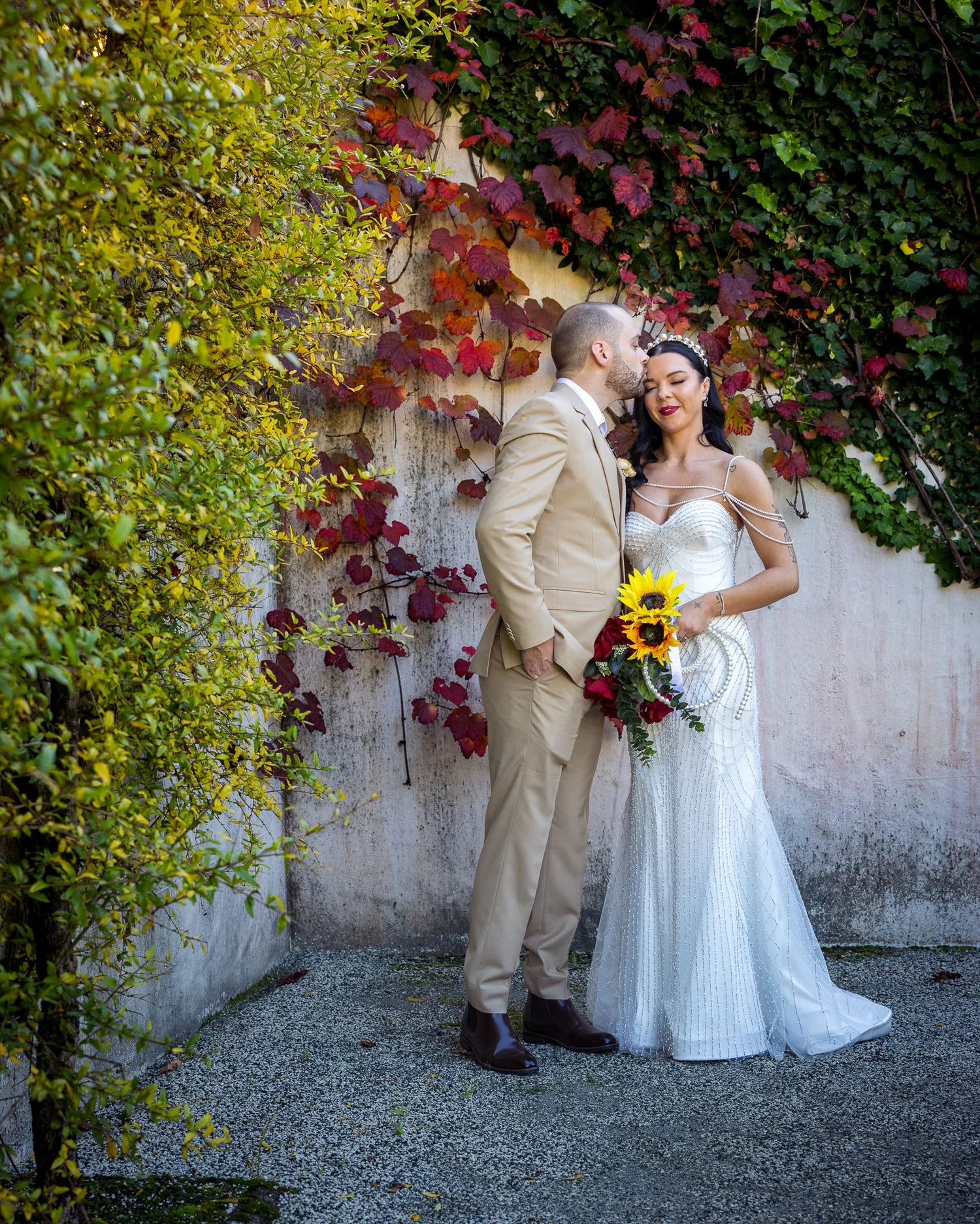 Emma and Corey stand against a wall of autumn leaves