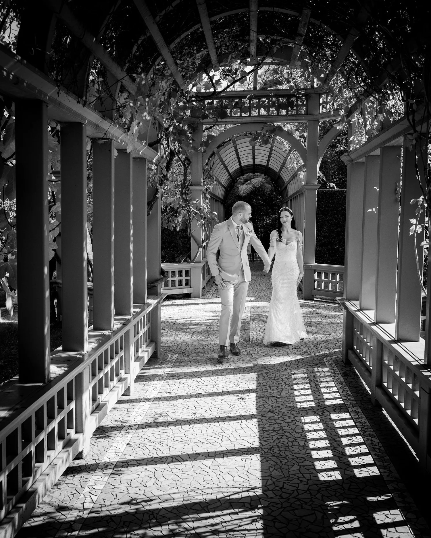 Black and white photo of Emma and Corey walking through a pergola